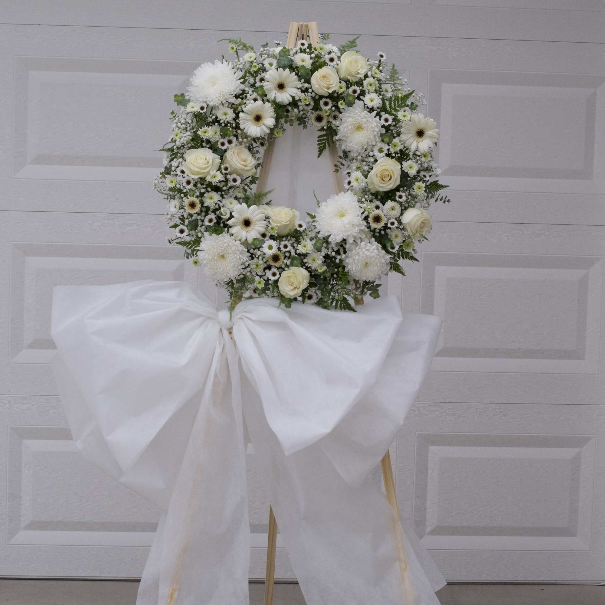 White floral wreath on a wooden easel with a large white bow