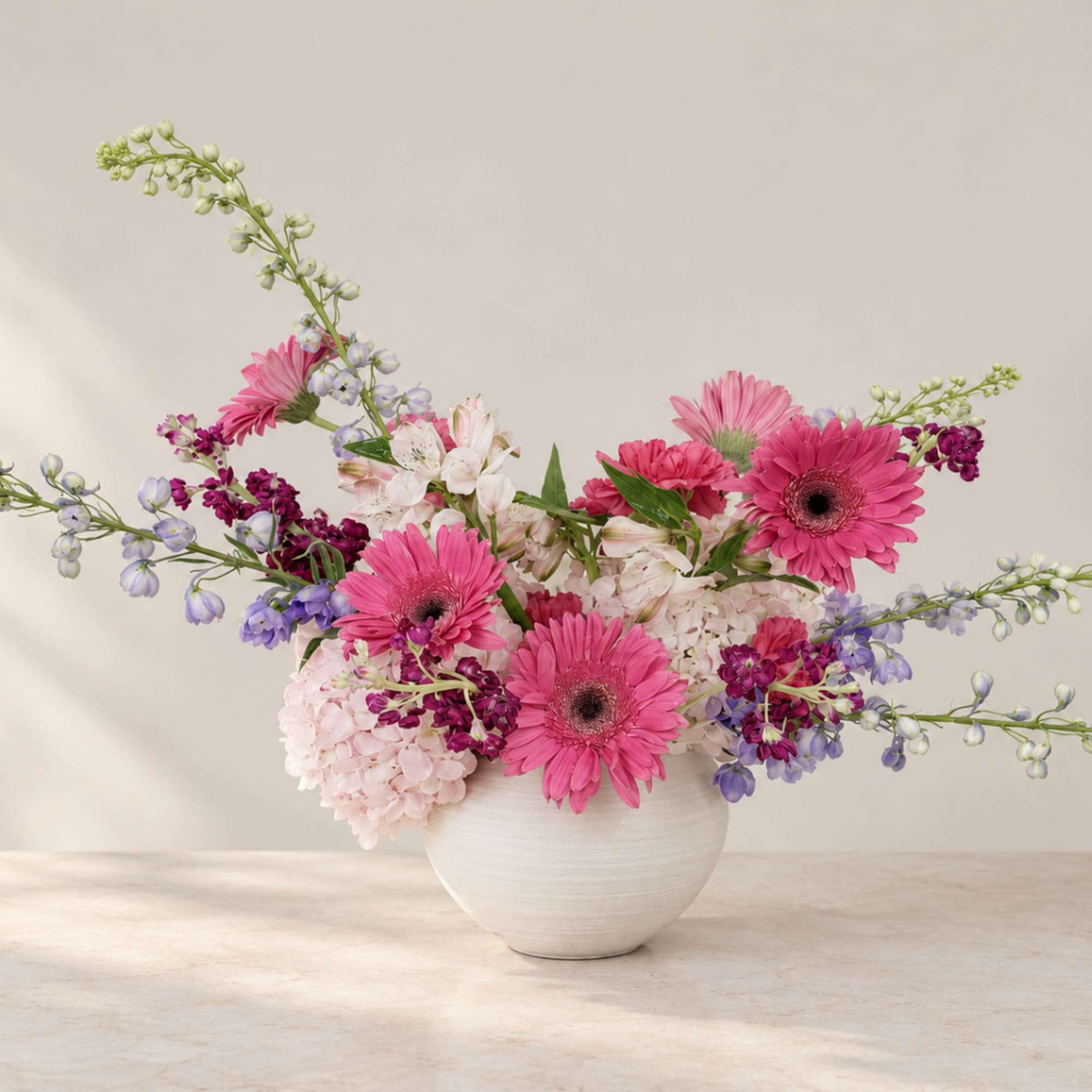 Pink gerbera daisies and mixed blooms in a white vase