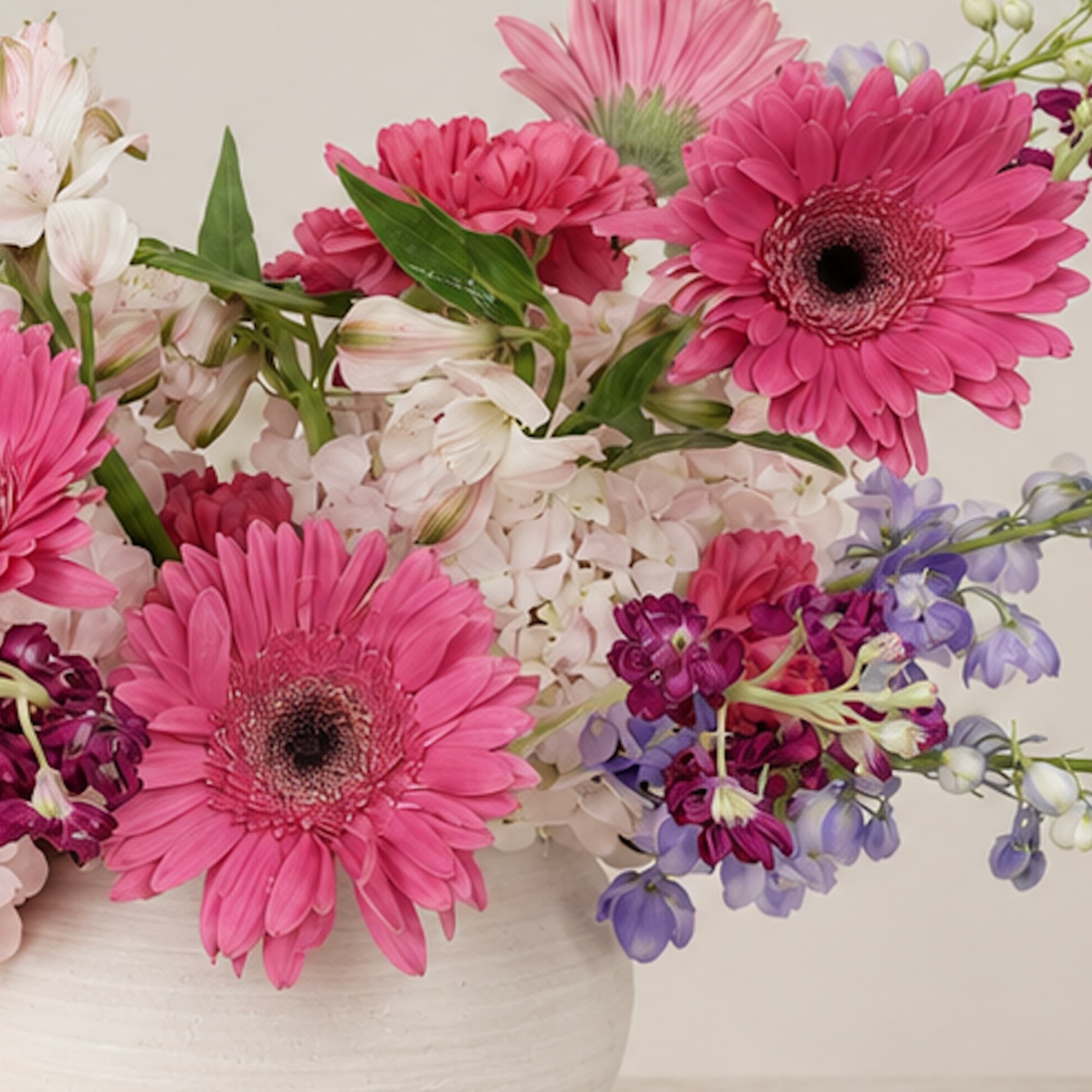 Pink gerbera daisies and mixed pastel flowers in a white vase