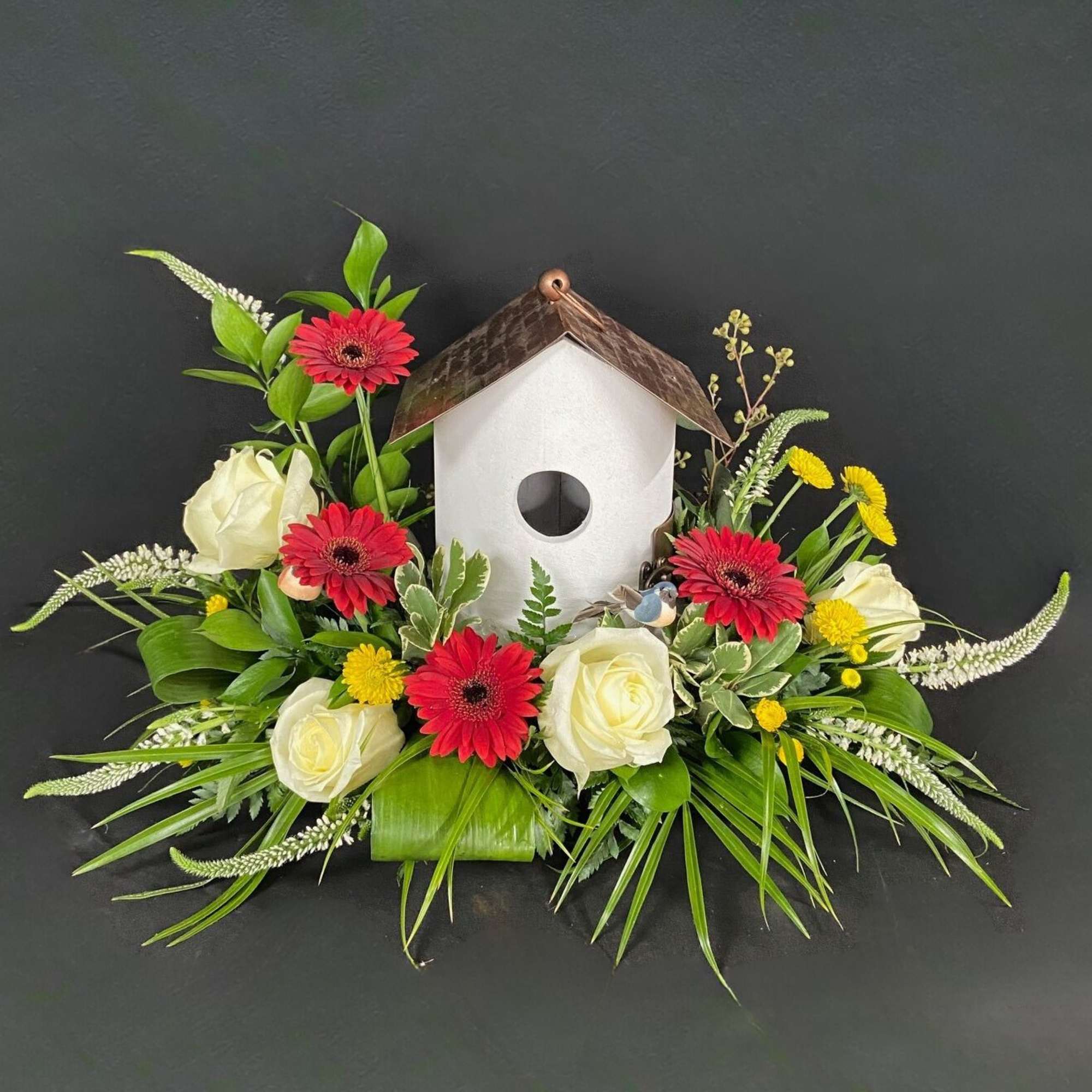 Floral arrangement around a white birdhouse with red and white flowers