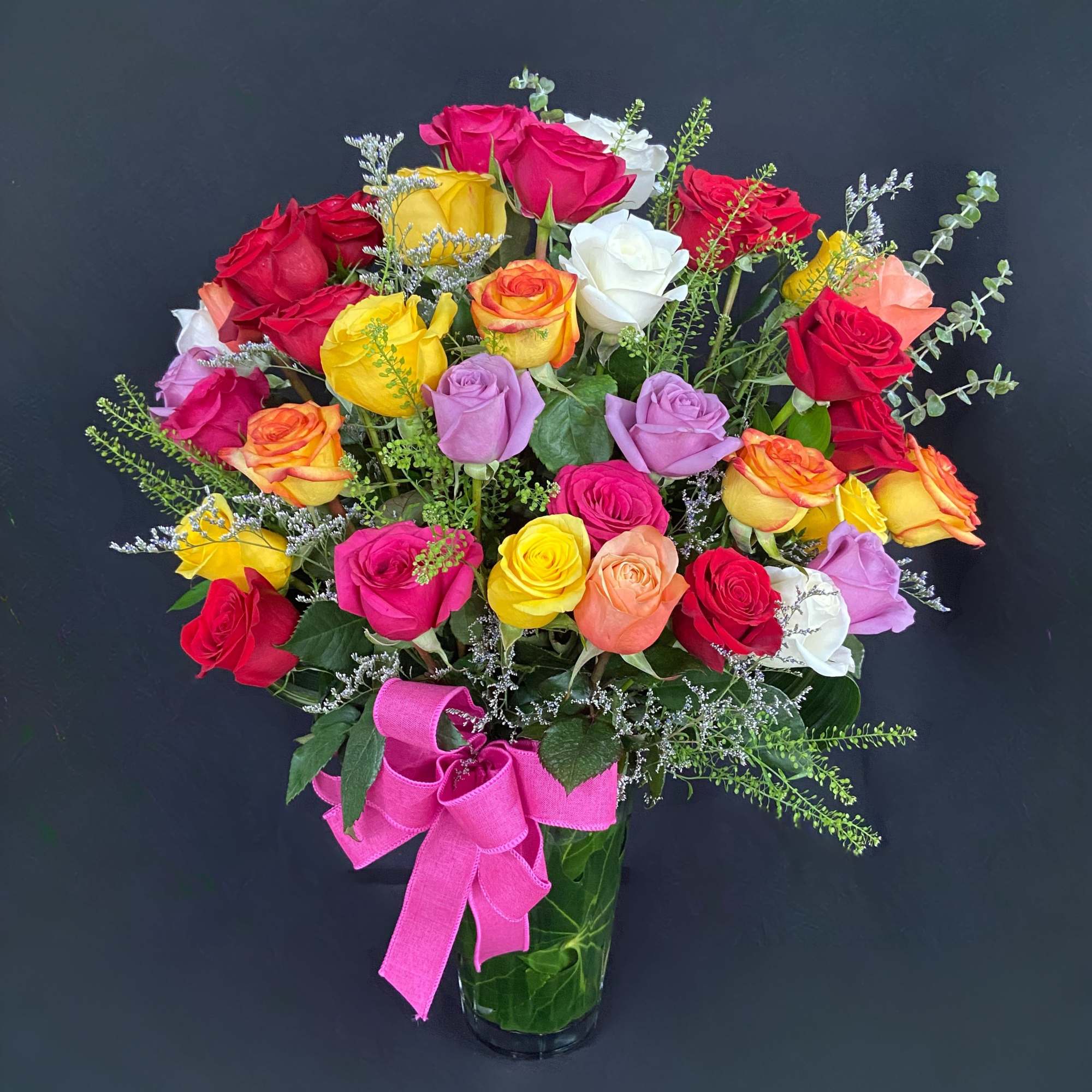 Colorful rose bouquet in a clear glass vase with a pink ribbon