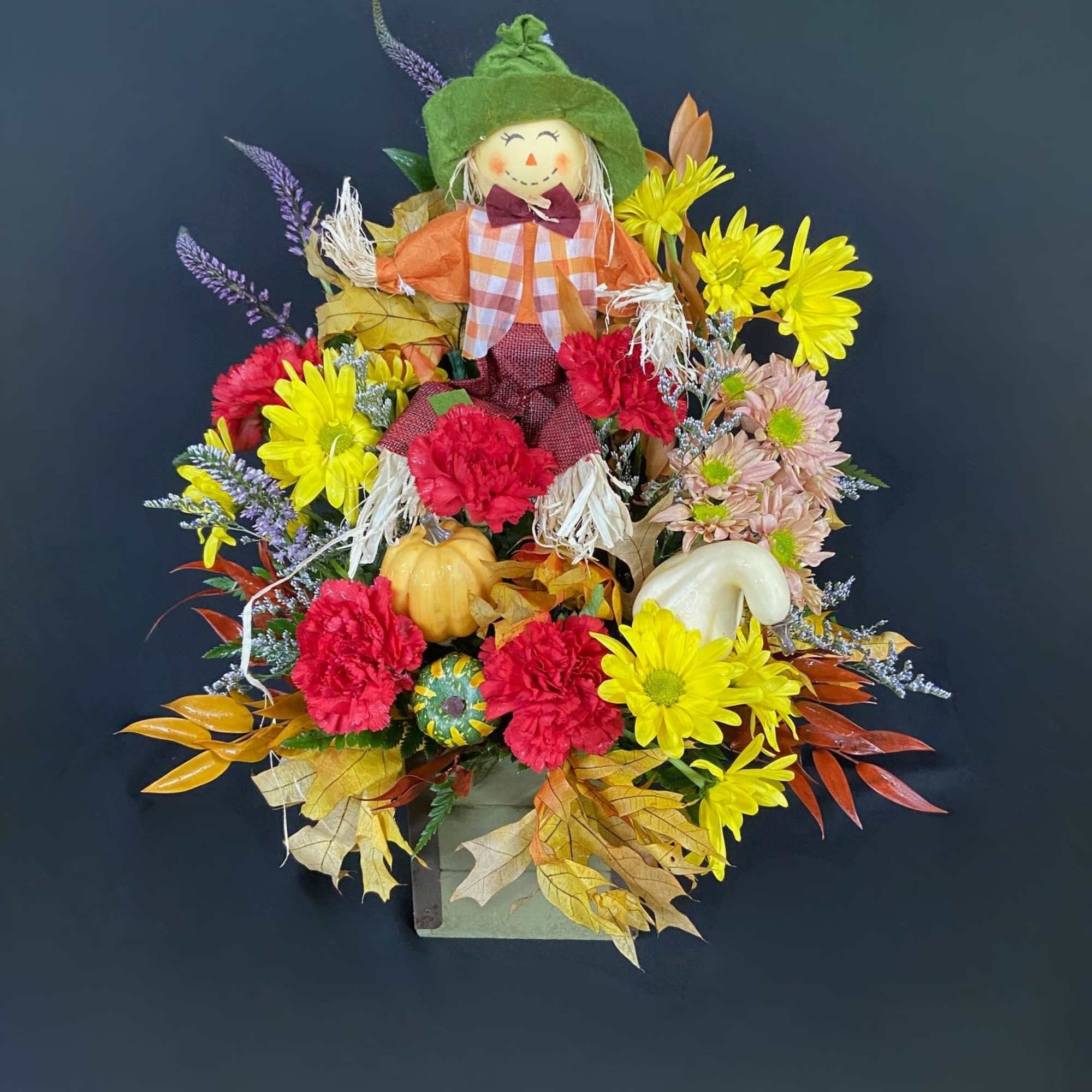 Fall floral arrangement with a scarecrow figure, chrysanthemums, and pumpkins