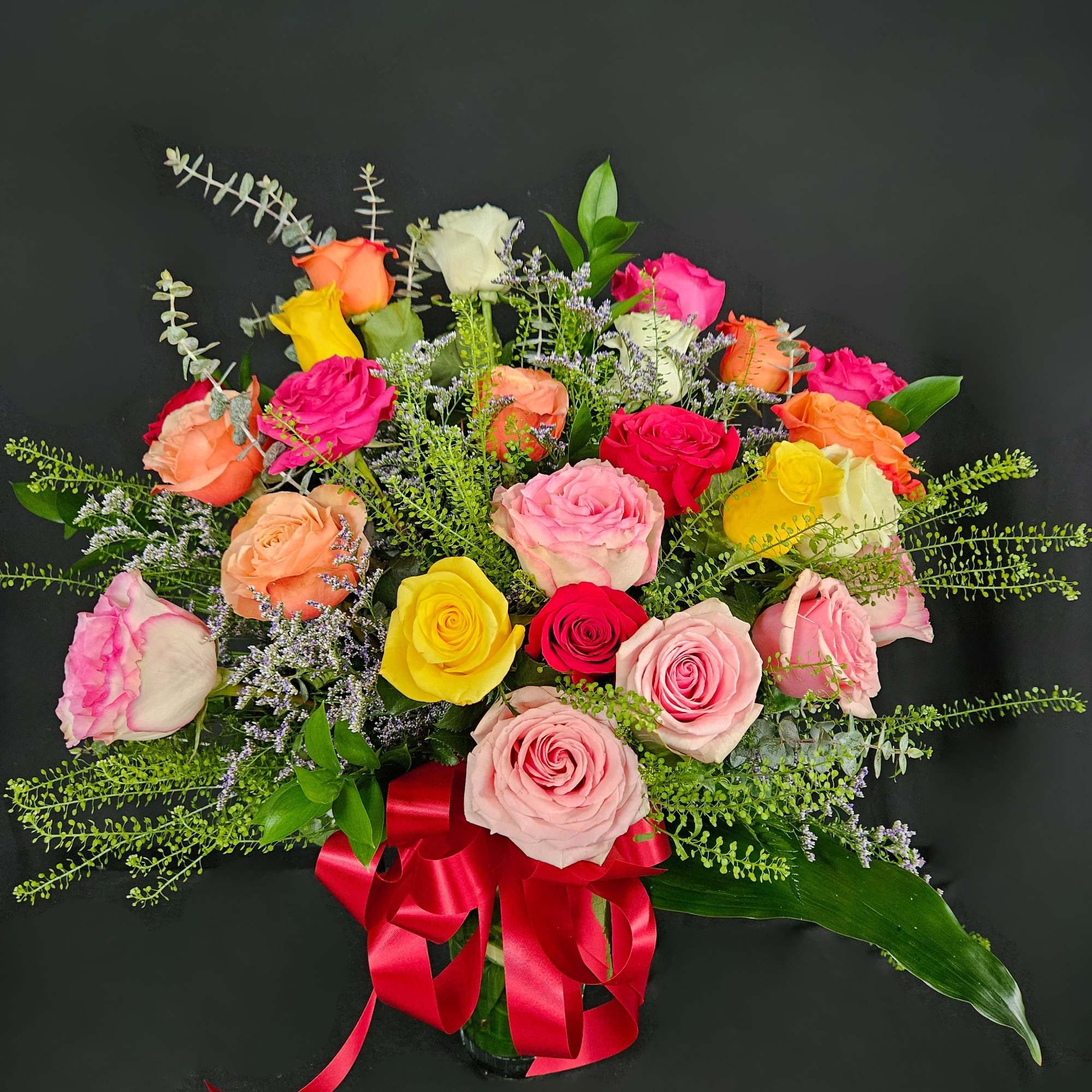 Mixed bouquet of colorful roses in a glass vase with a red ribbon