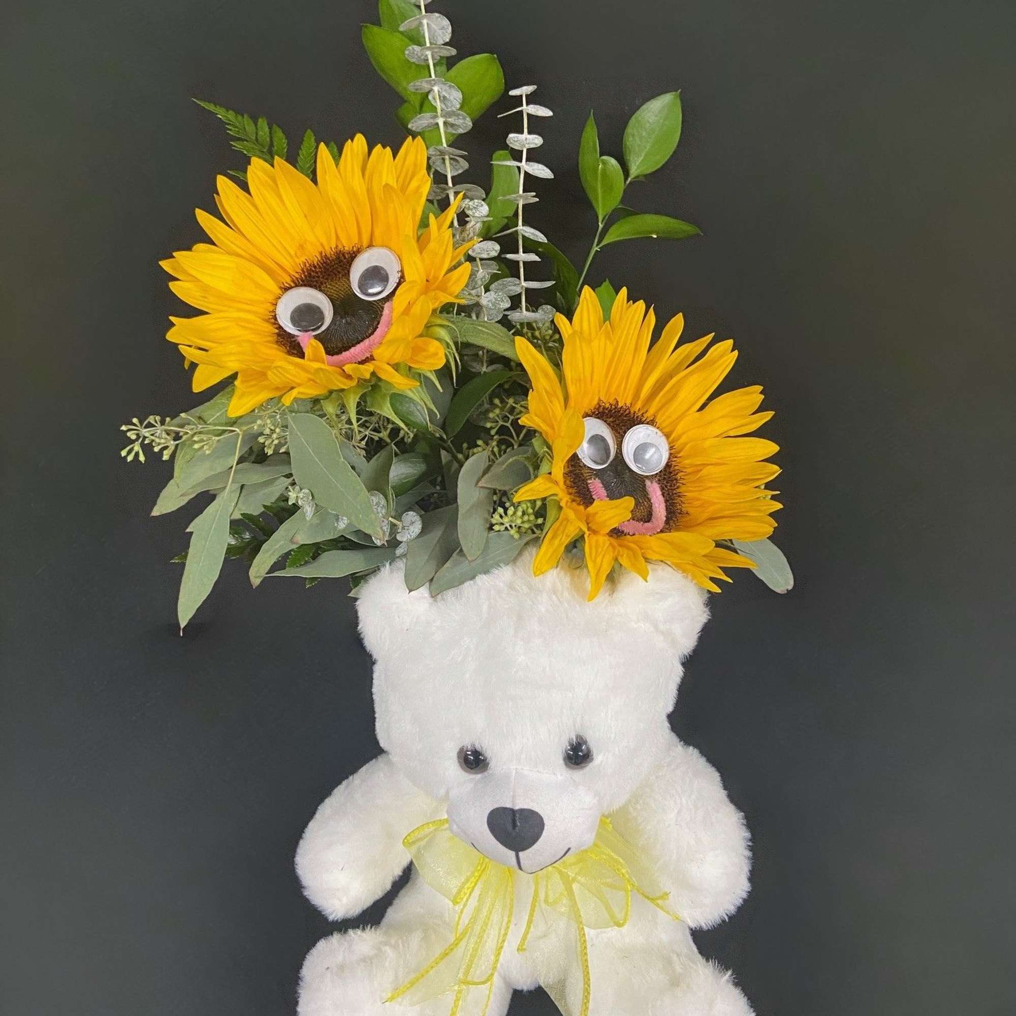 White teddy bear with a sunflower arrangement on its head