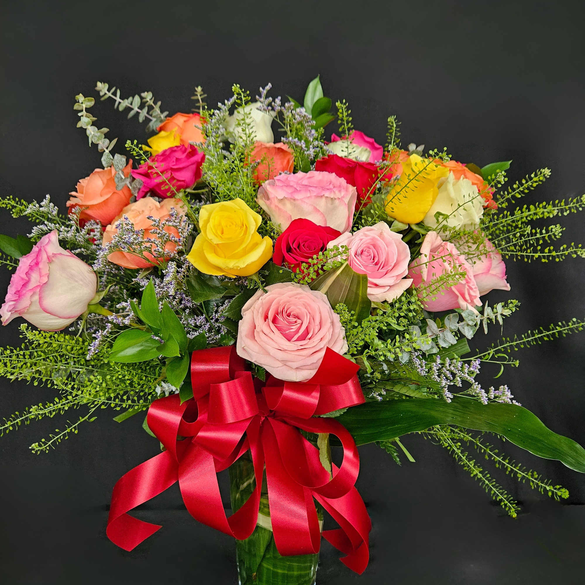 Mixed roses in a glass vase with a red ribbon bow