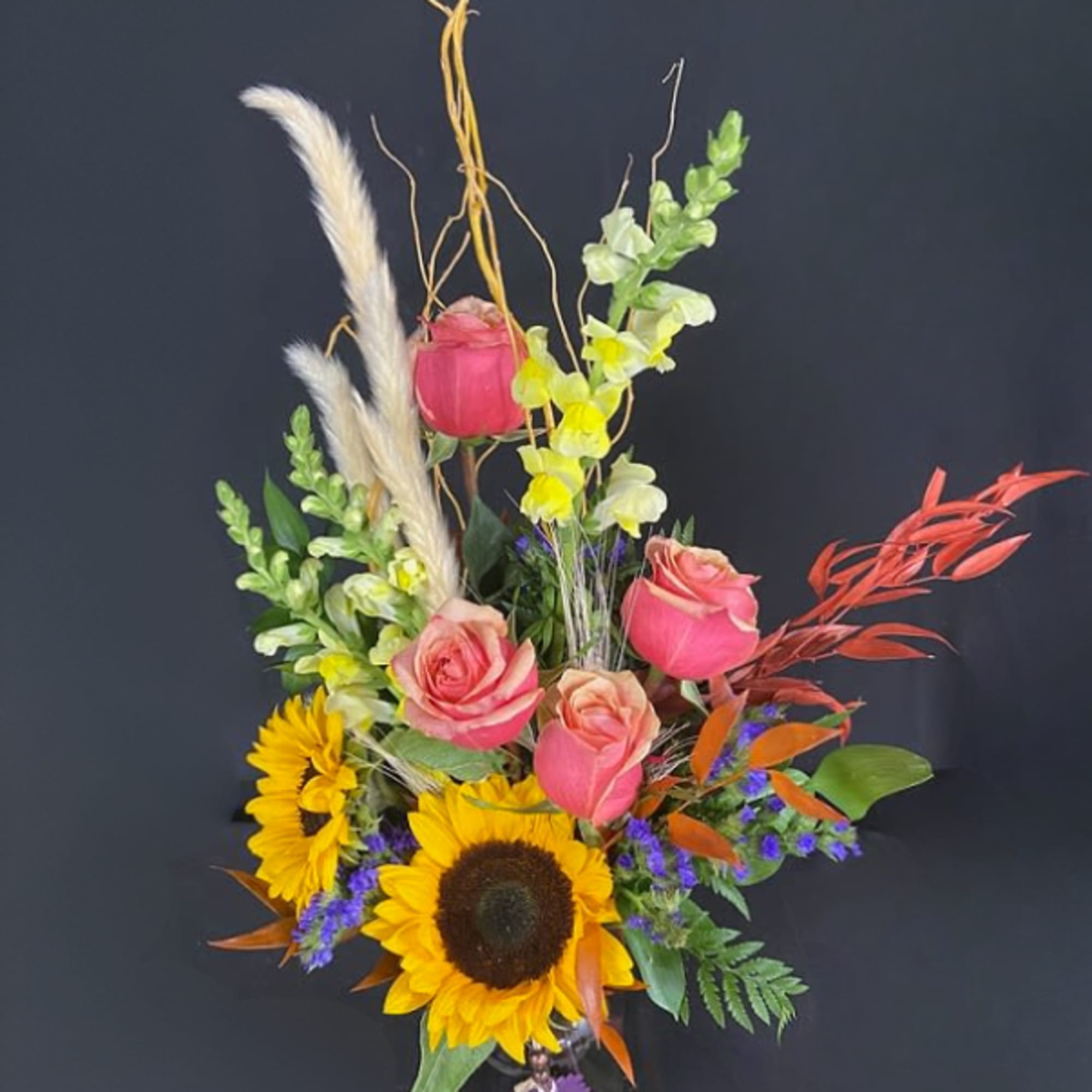 Bouquet with sunflowers, pink roses, and yellow snapdragons in a glass vase