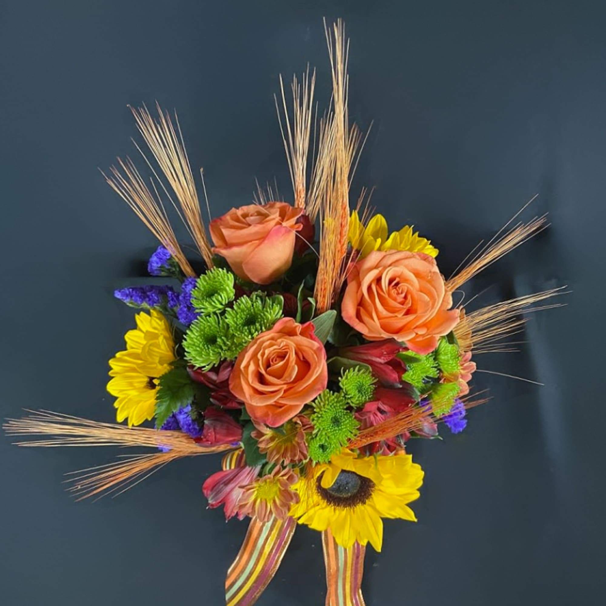 Bouquet of orange roses, yellow sunflowers, and mixed blooms with decorative grasses