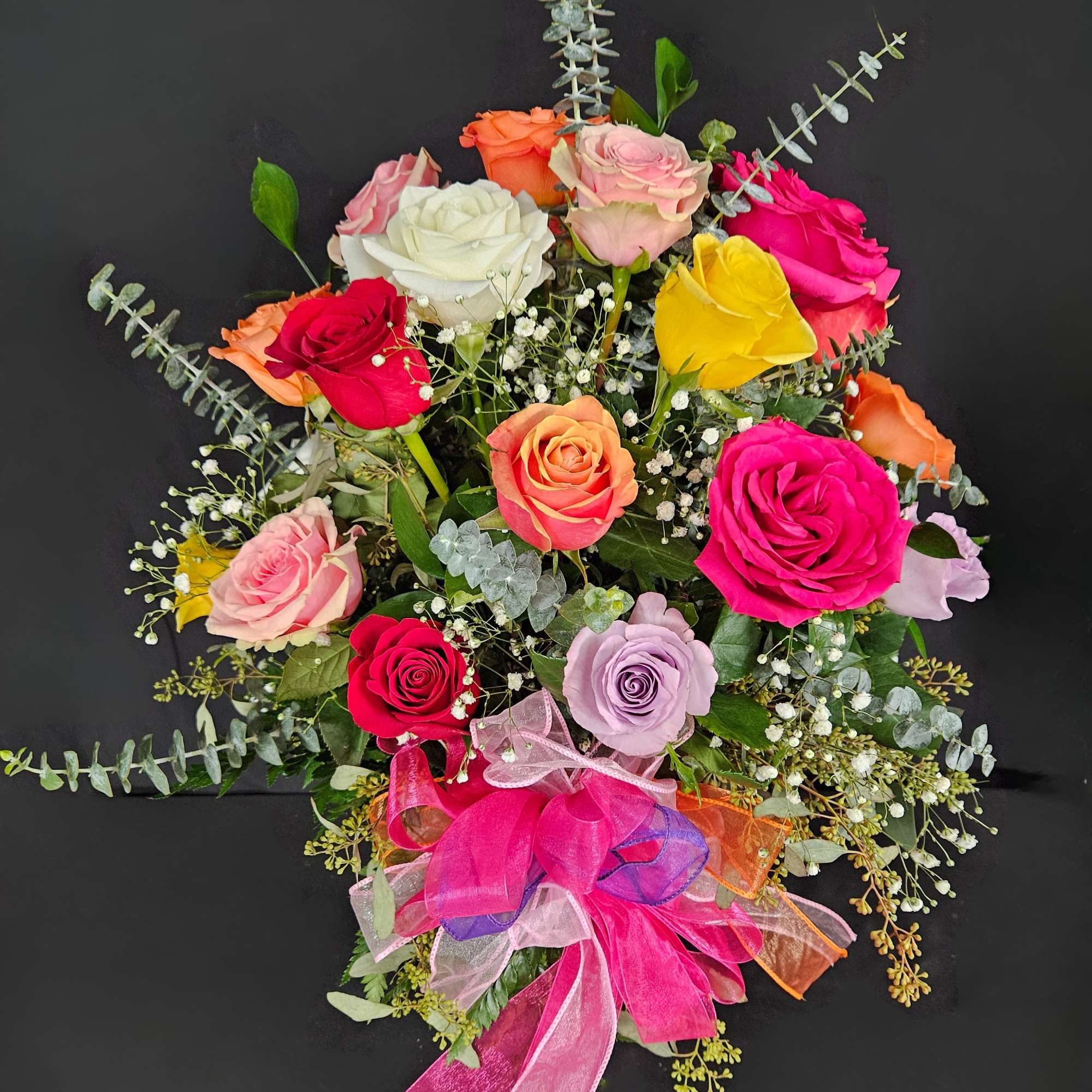 Mixed arrangement of colorful roses with baby's breath and a bright pink bow on a dark background