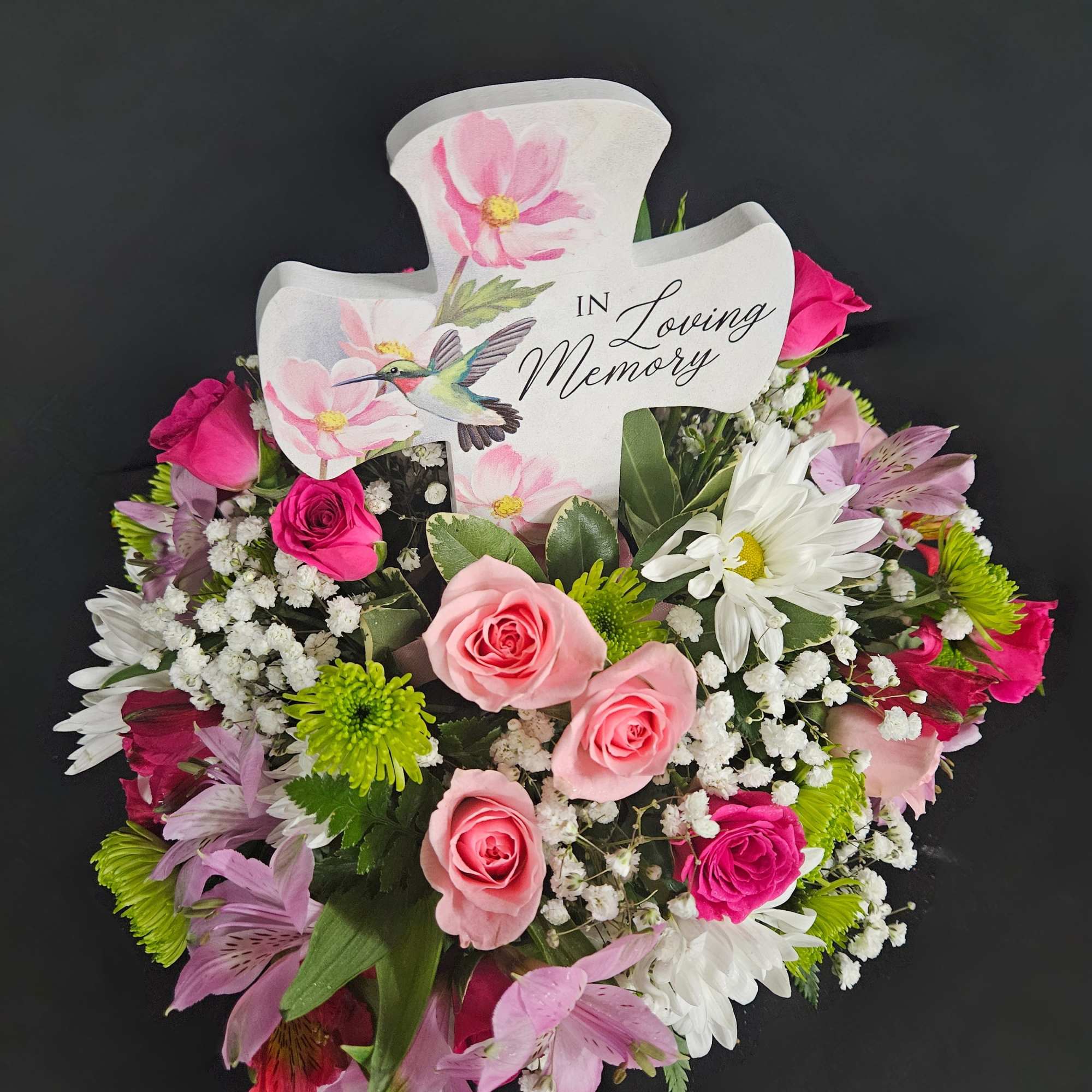 Sympathy floral arrangement with pink roses and white daisies around an "In Loving Memory" cross