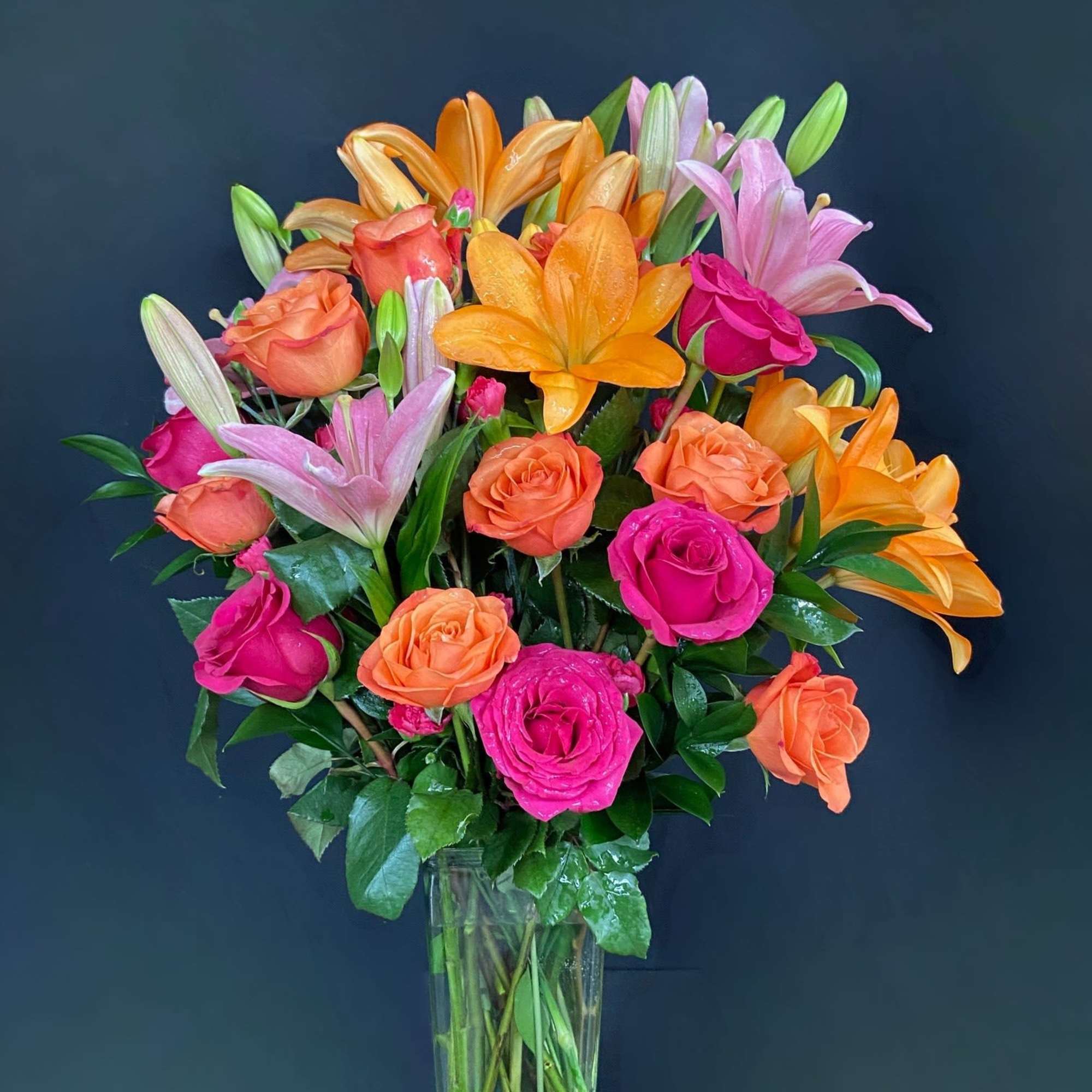 Mixed bouquet of orange and pink roses with lilies in a clear glass vase