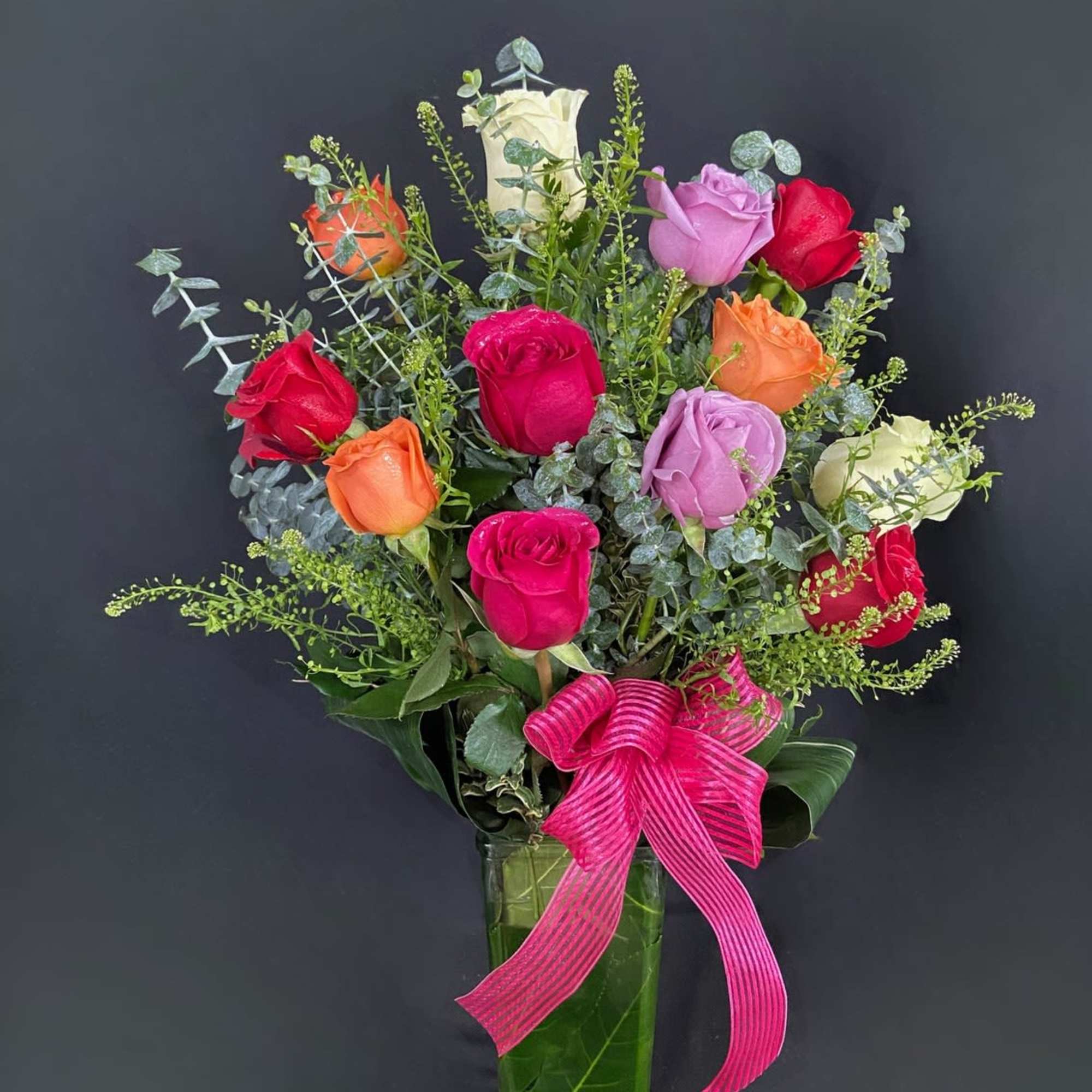 Mixed roses in a tall glass vase with a pink ribbon bow