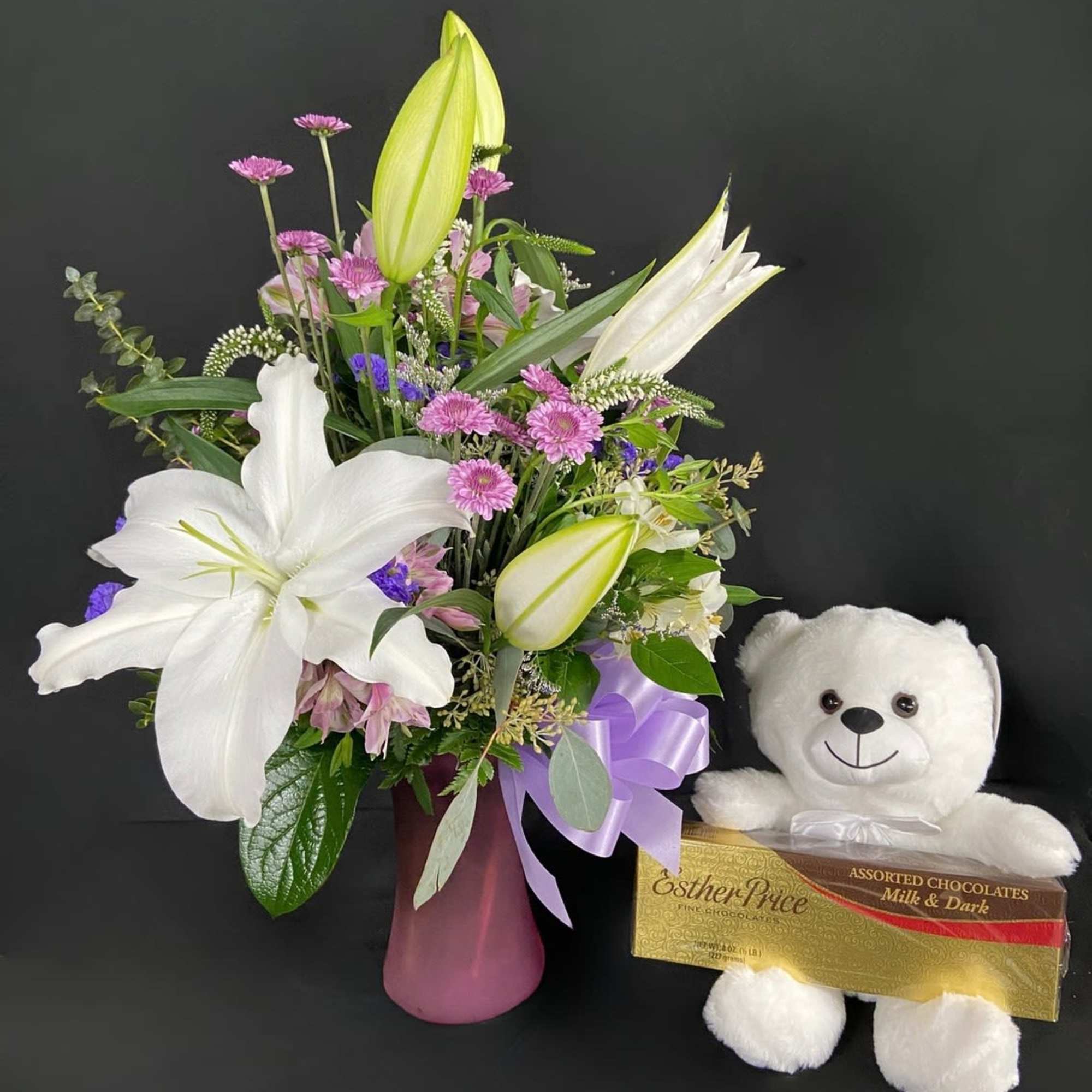 Bouquet of white lilies and pink flowers in a vase with a teddy bear and chocolates