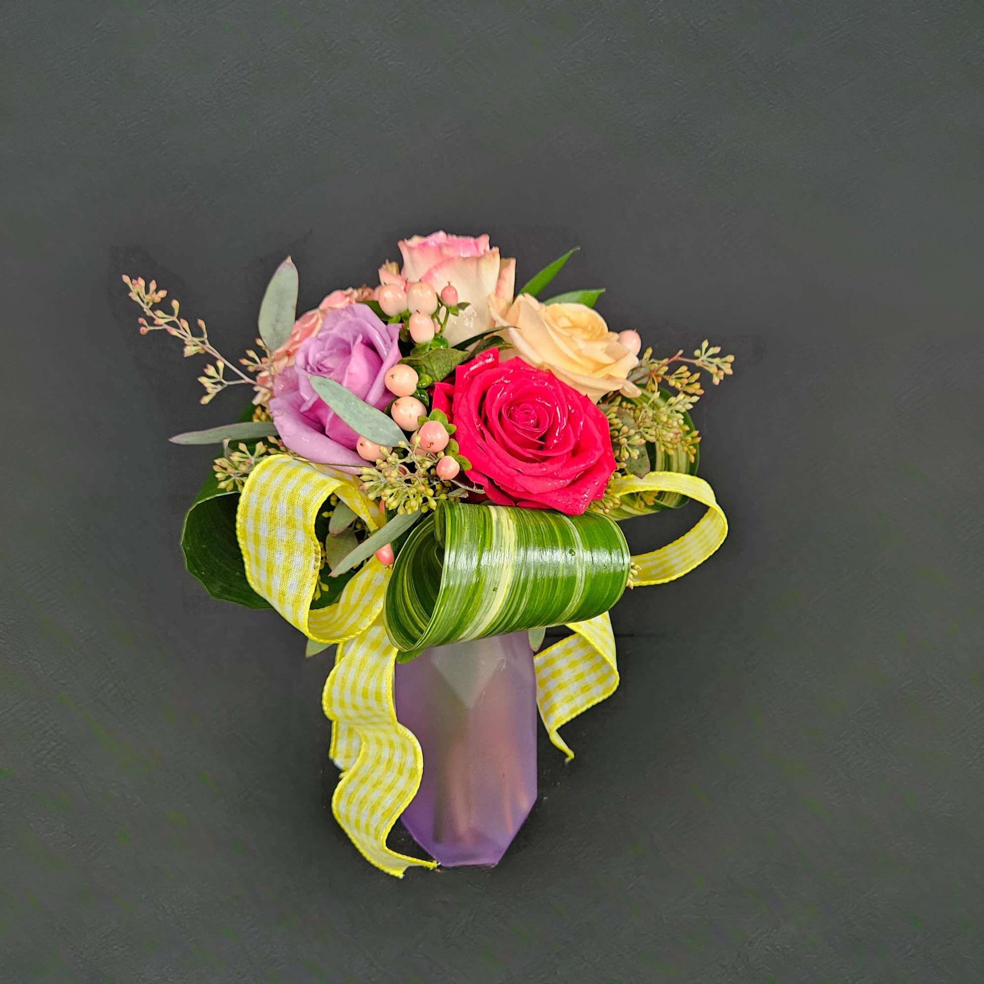 Small arrangement of multicolored roses with berries and yellow ribbon in a purple vase