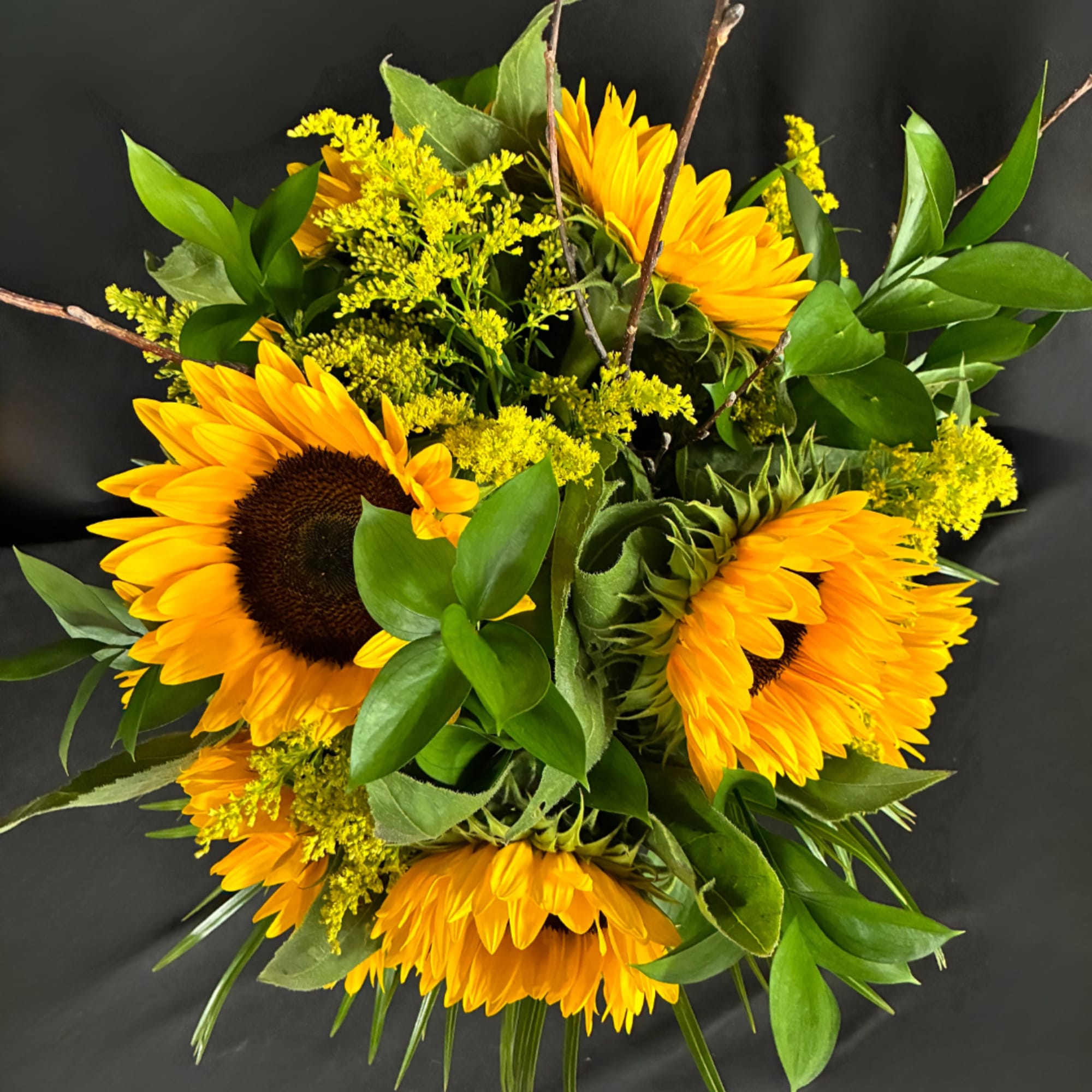 Bouquet of yellow sunflowers with green foliage on a dark background