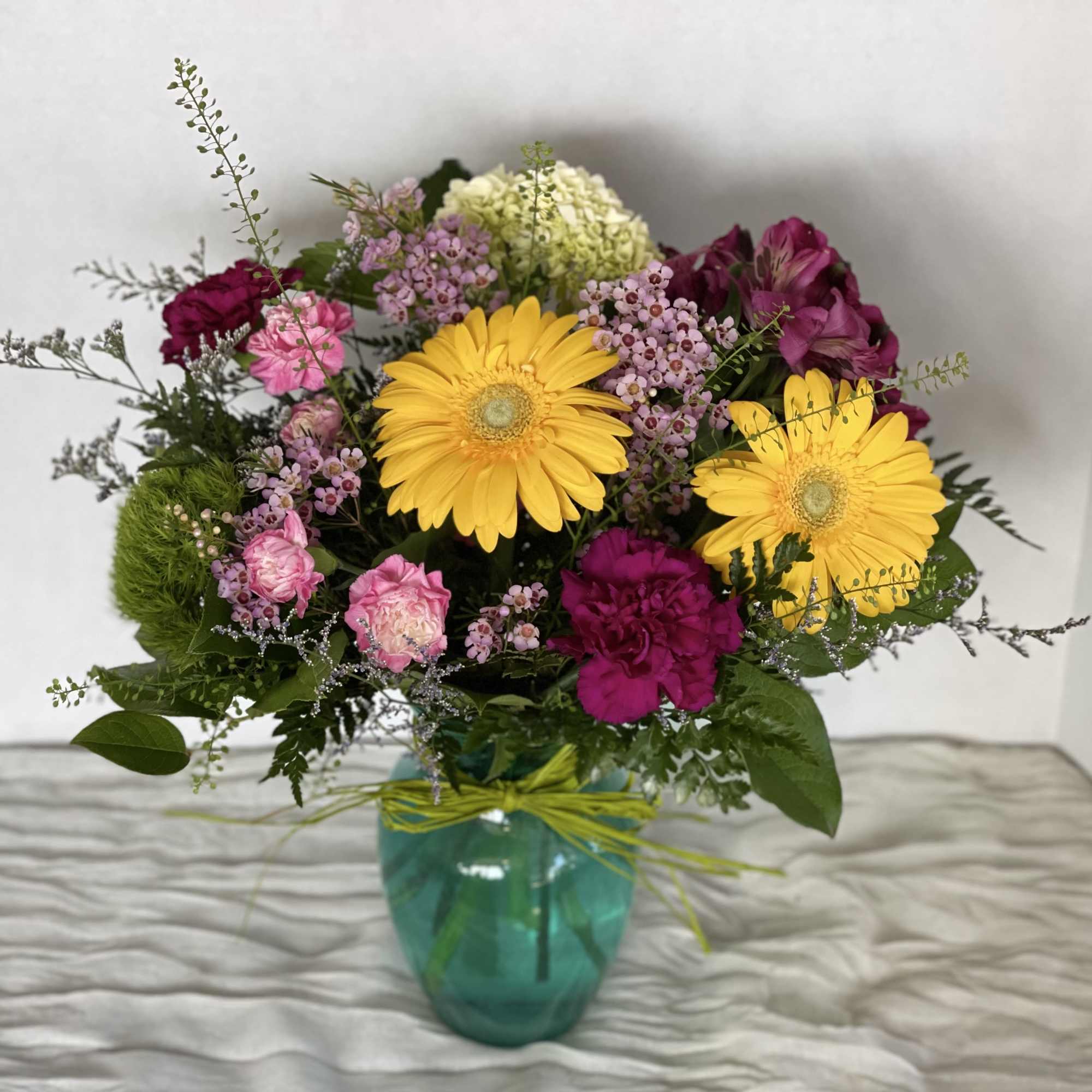 Mixed bouquet with yellow daisies and pink flowers in a teal vase
