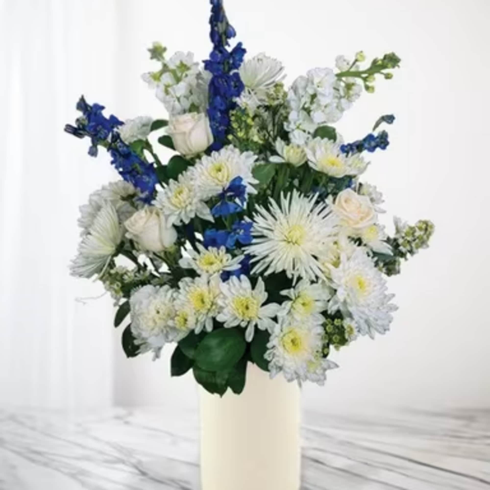 White and blue floral arrangement in a cream vase