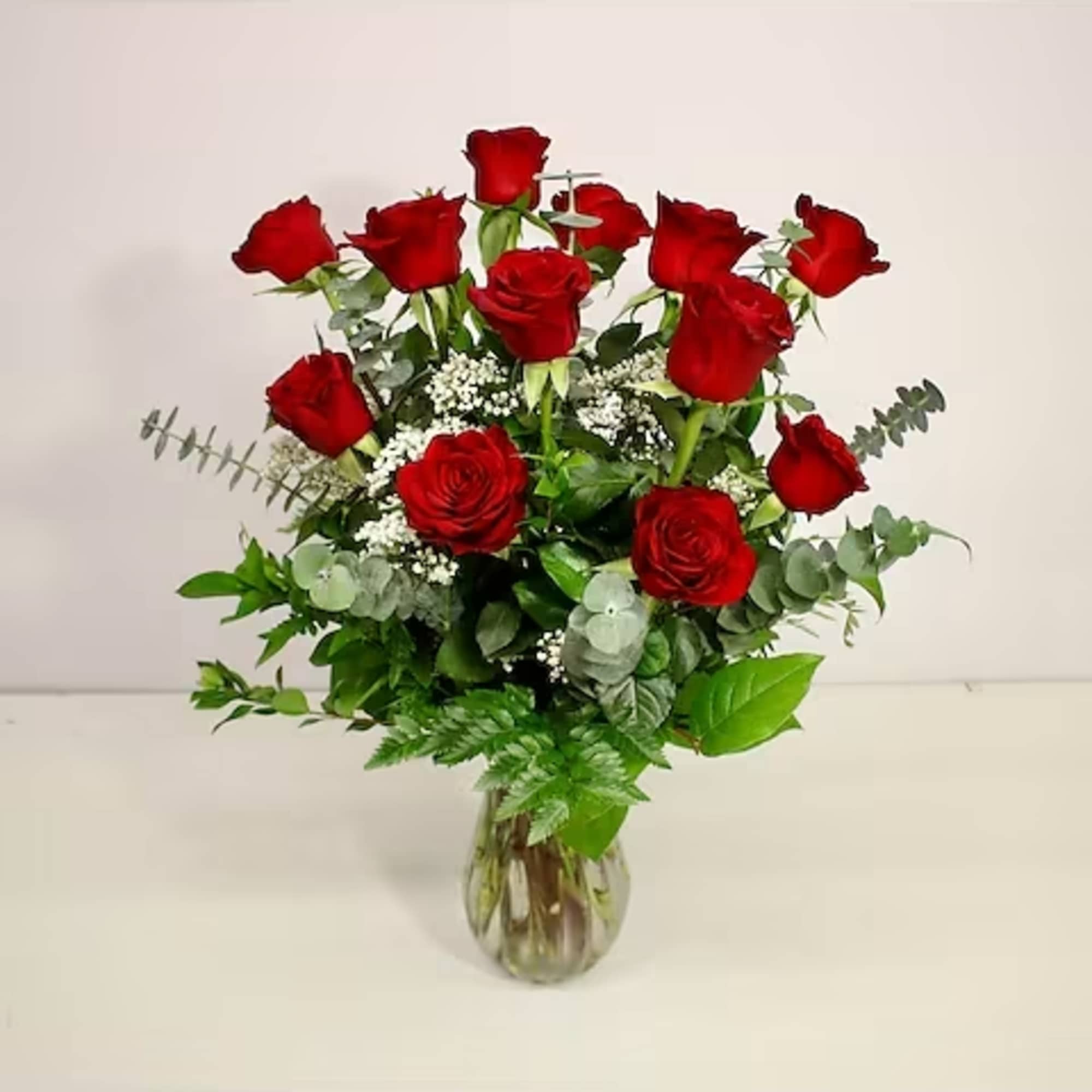 Red roses arranged in a clear glass vase with mixed greenery