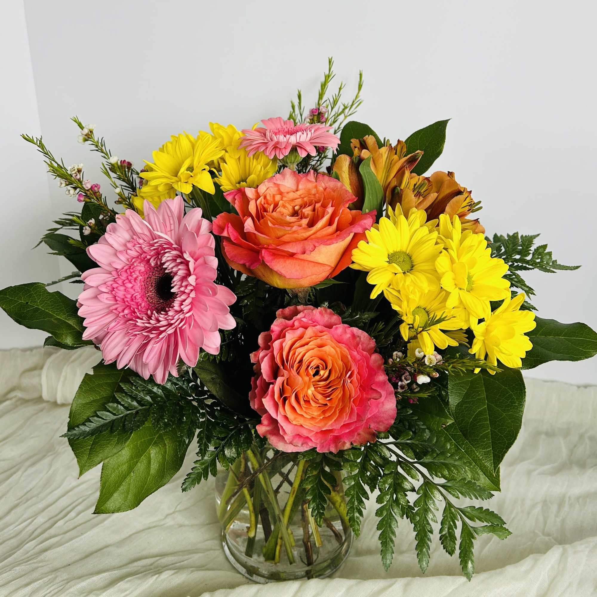 Mixed bouquet of pink, yellow, and orange flowers in a clear glass vase