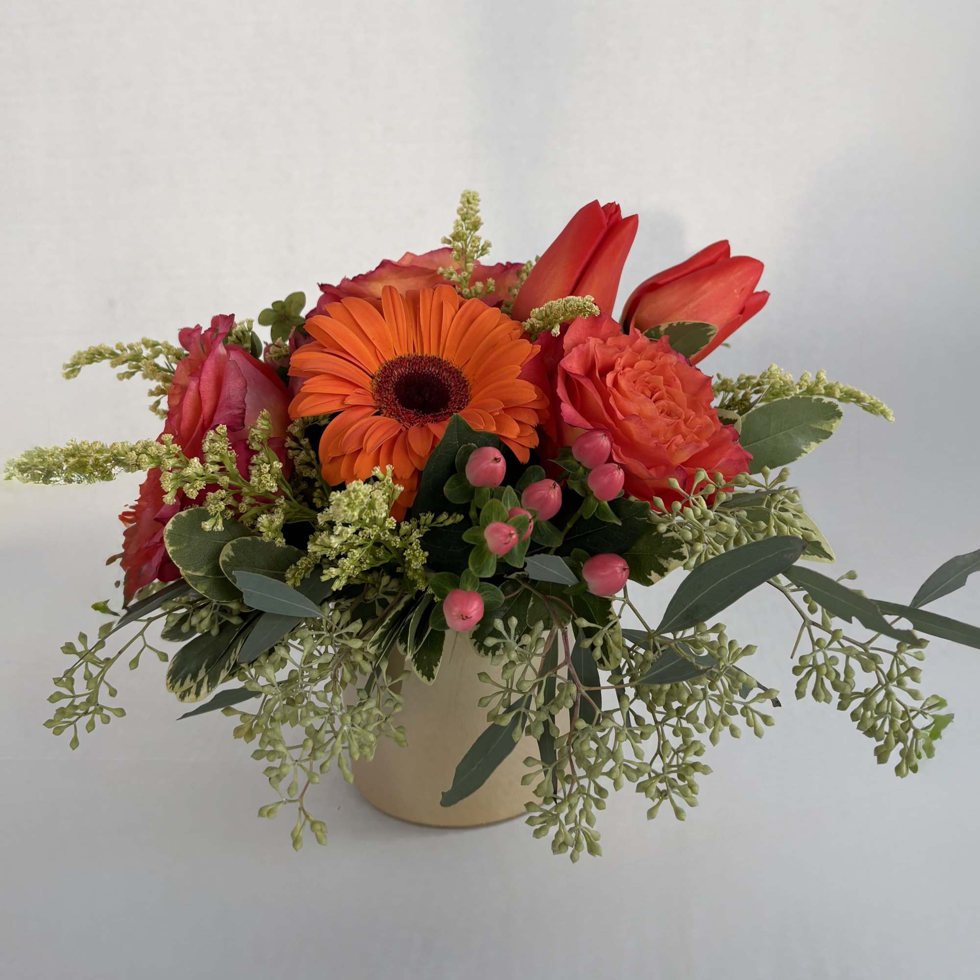 Bright mixed flower arrangement in a beige vase with orange and red blooms