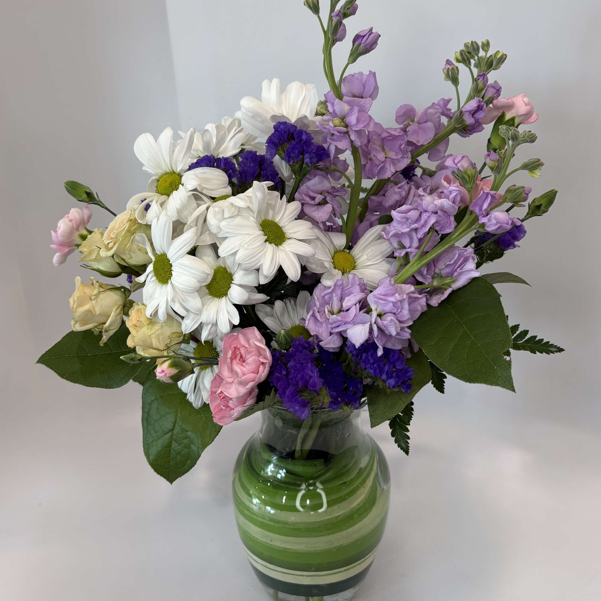 Bouquet of white daisies, lavender blooms, and pink flowers in a glass vase