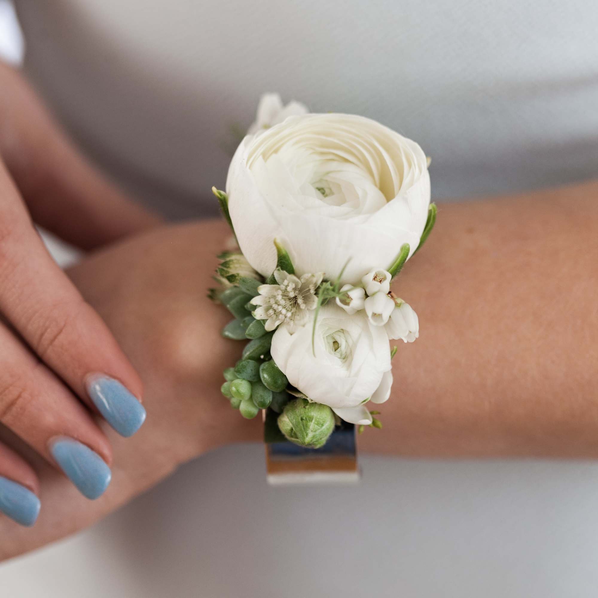 Cuff corsage featuring ranunculus with bits of foliage and other filler flowers.
