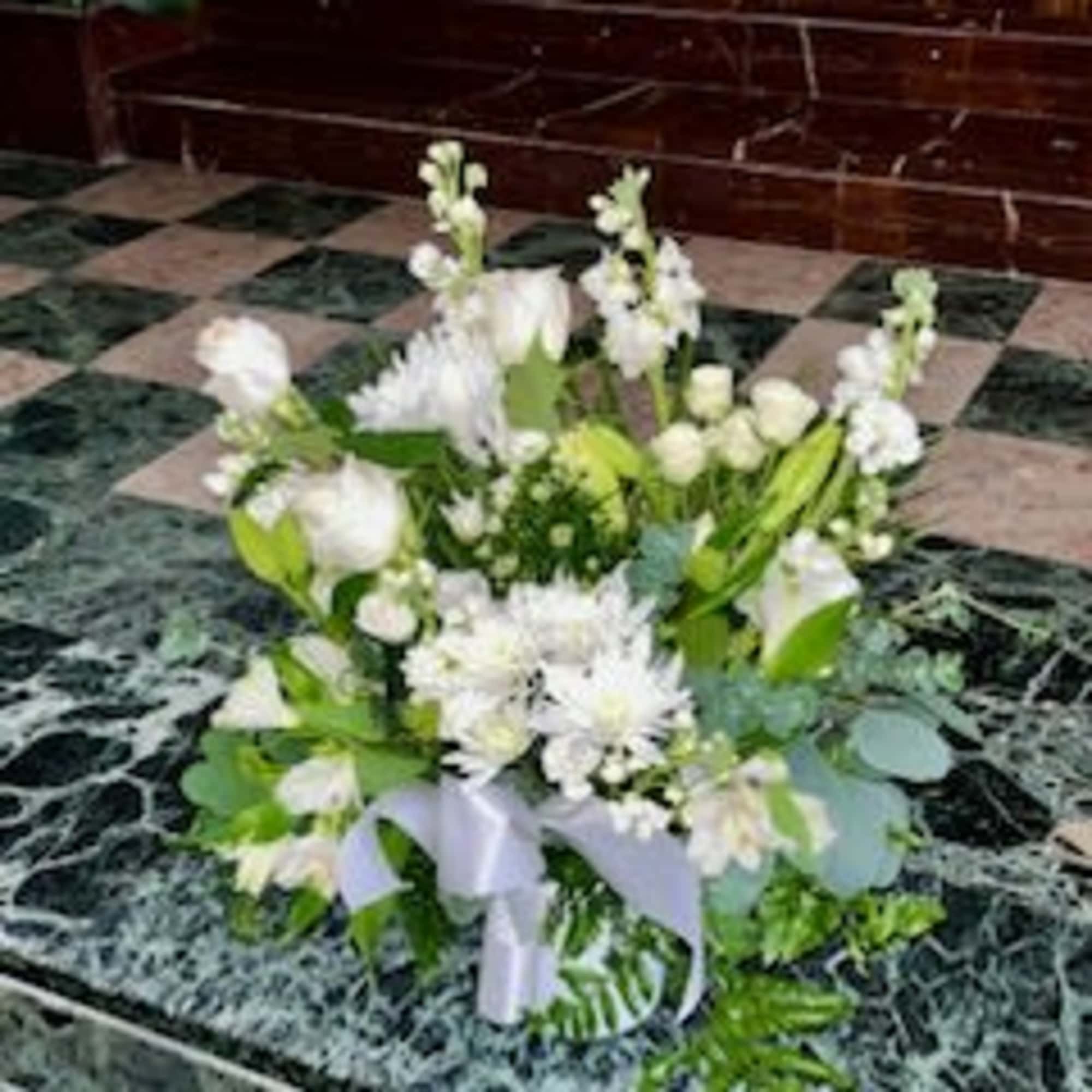 White floral arrangement with a lavender ribbon on a marble floor