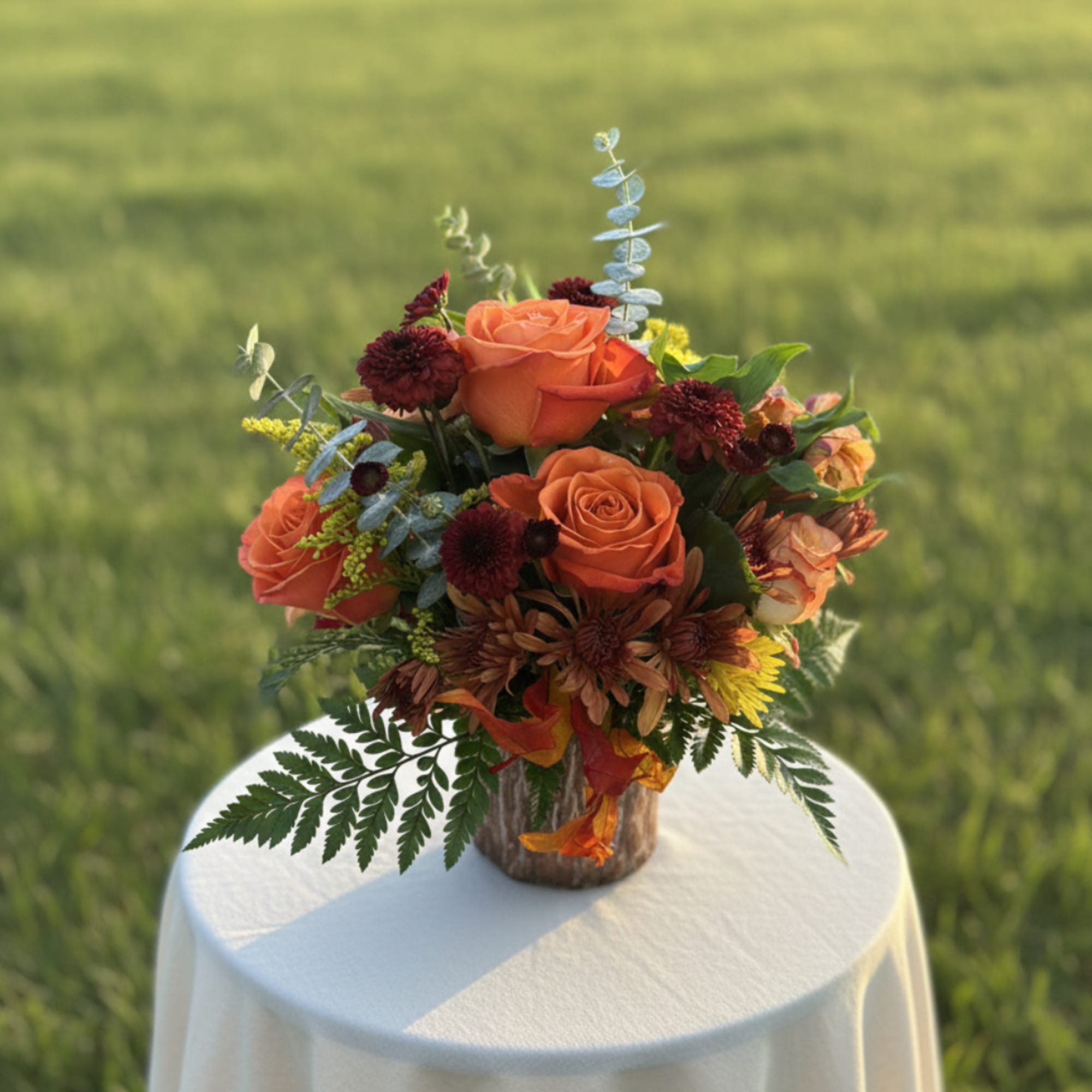 Orange rose bouquet in a rustic vase on a draped table