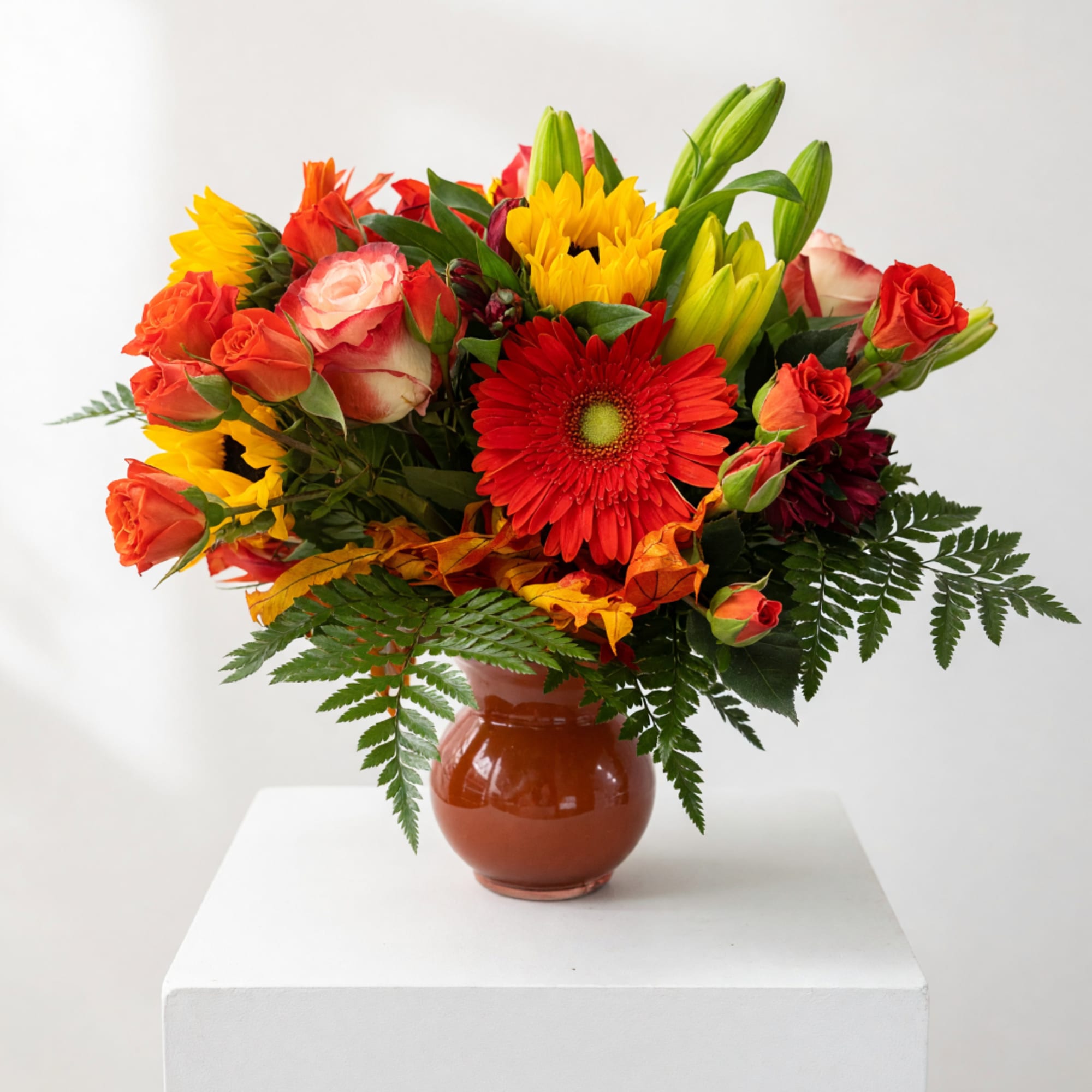 Mixed bouquet of roses, lilies, and gerbera daisies in a brown vase