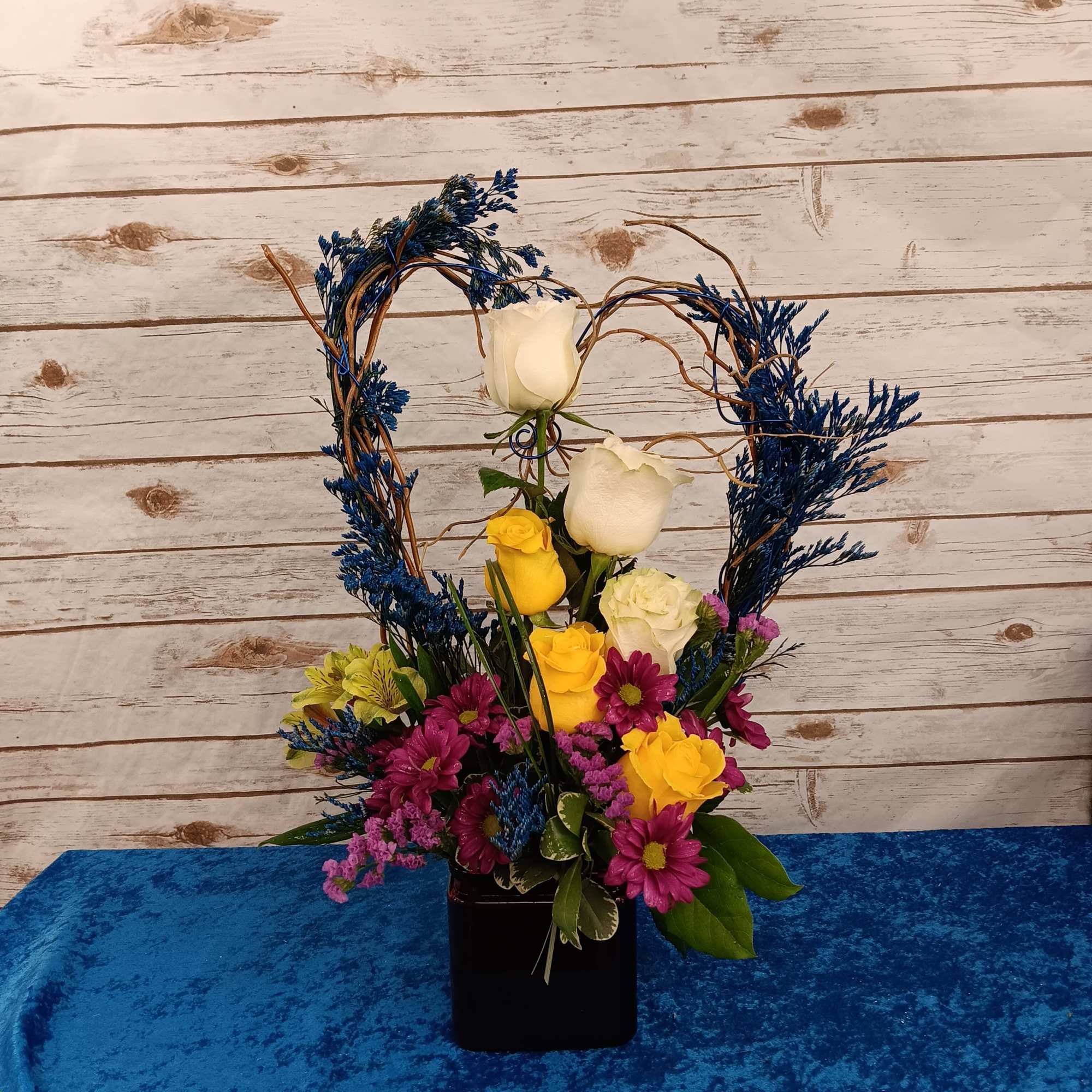 Heart-shaped floral arrangement with roses and daisies in a black vase