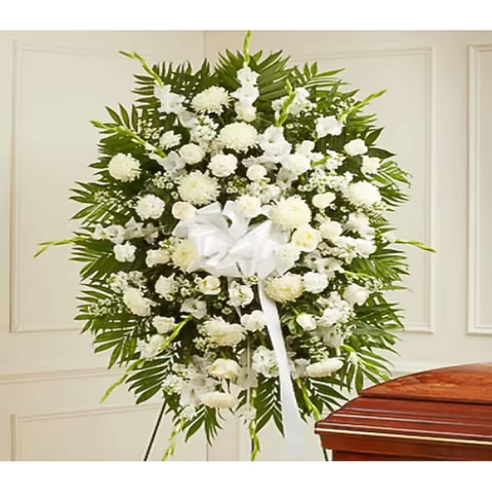 White funeral spray with a ribbon on a stand beside a casket
