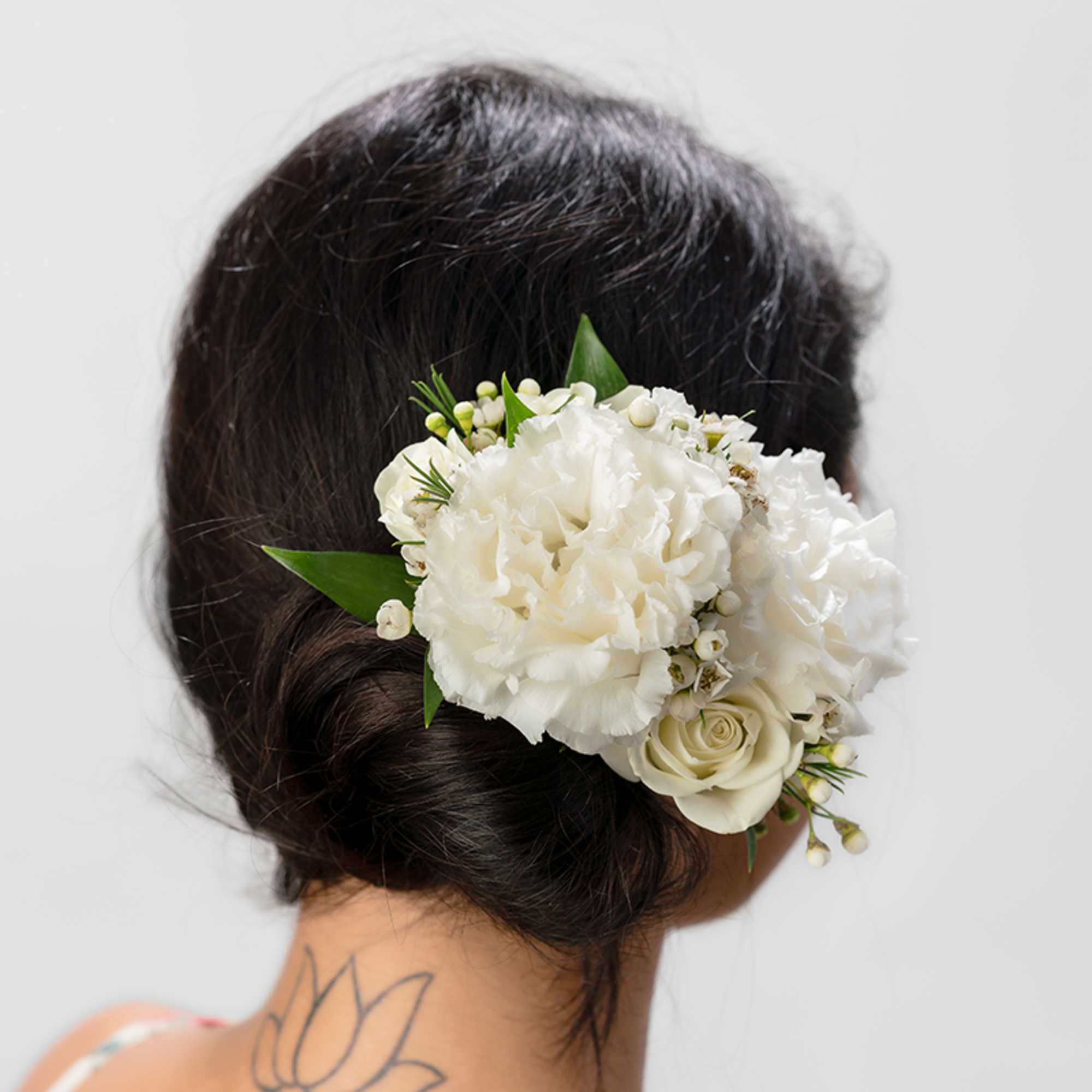 White carnation and rose hair floral piece worn above a low dark bun, viewed from the back