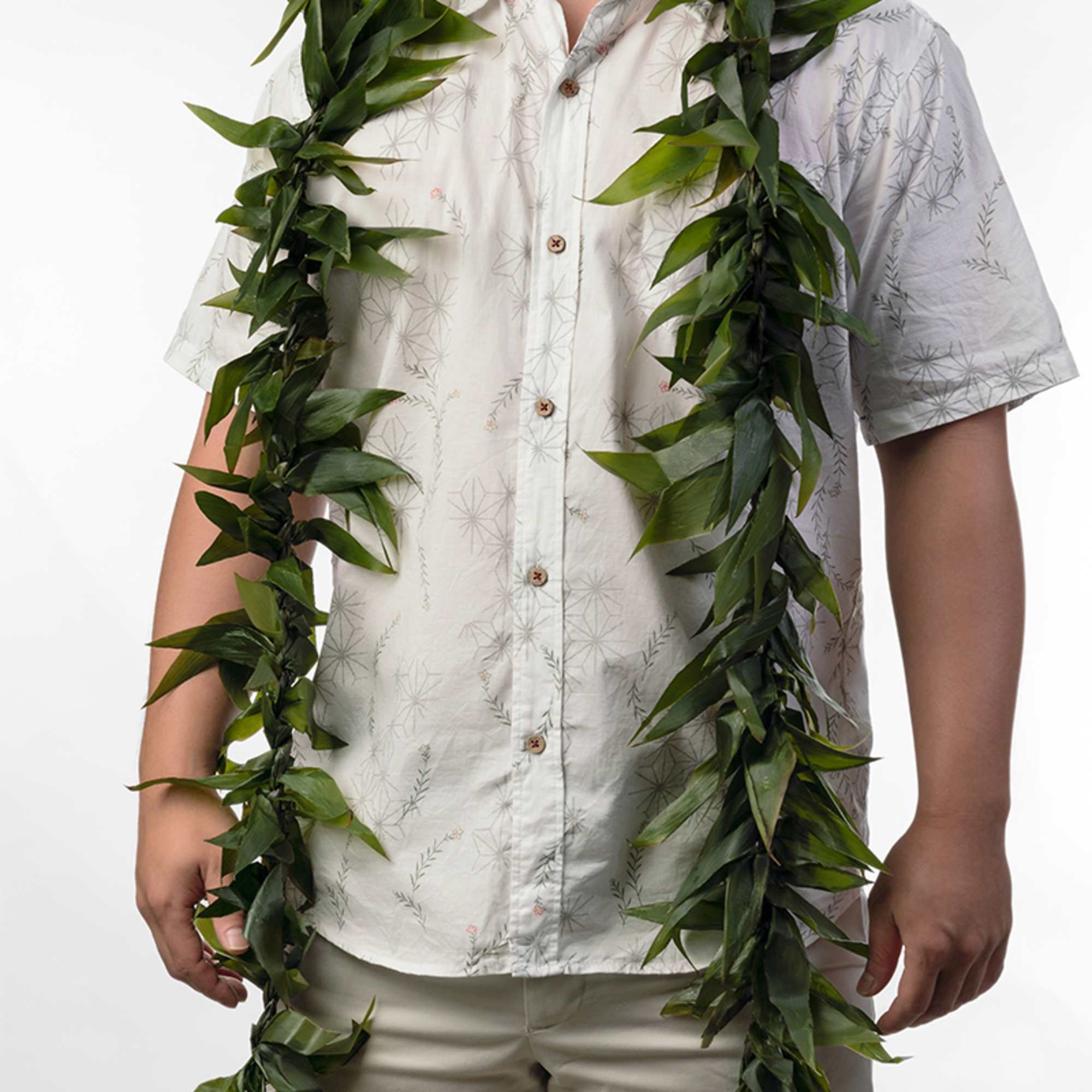 Person wearing a long green leaf lei over a white short-sleeve shirt