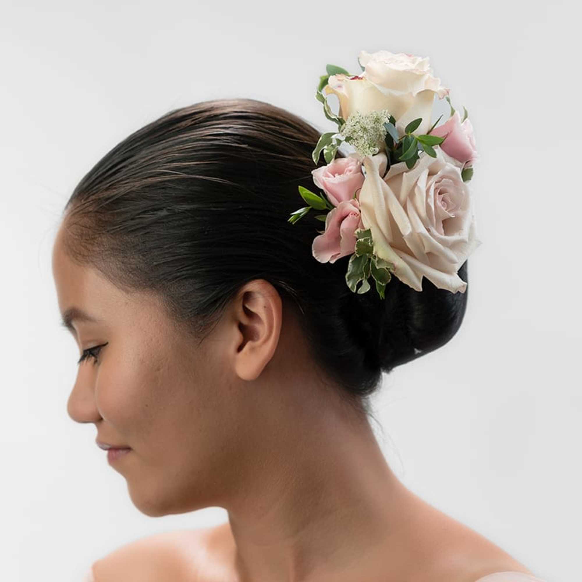 Floral hairpiece of ivory and blush roses worn on a sleek low bun