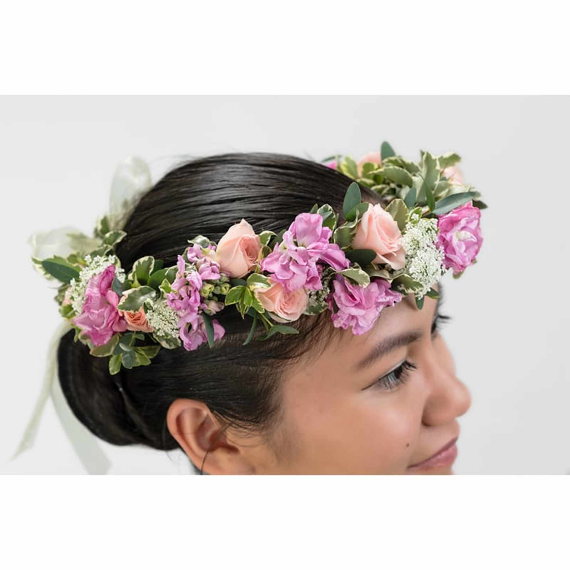 Pink and peach flower crown with small blooms and ribbon worn on a woman's head in profile.