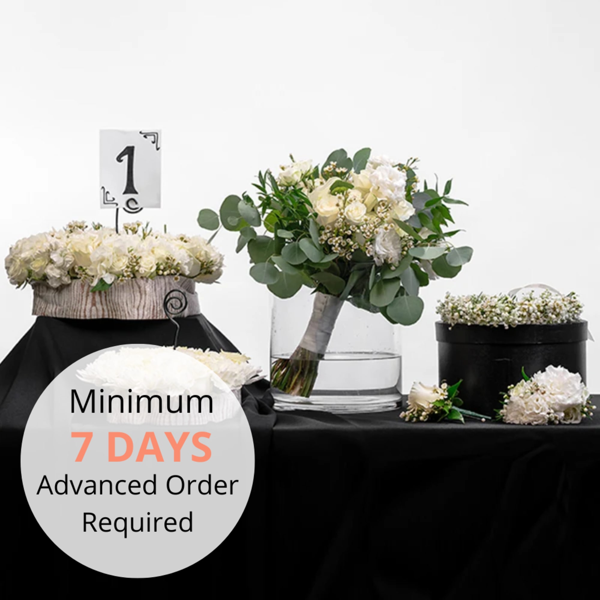 Coordinated white rose wedding set with bouquet, centerpiece, and floral accents on a black-draped table.