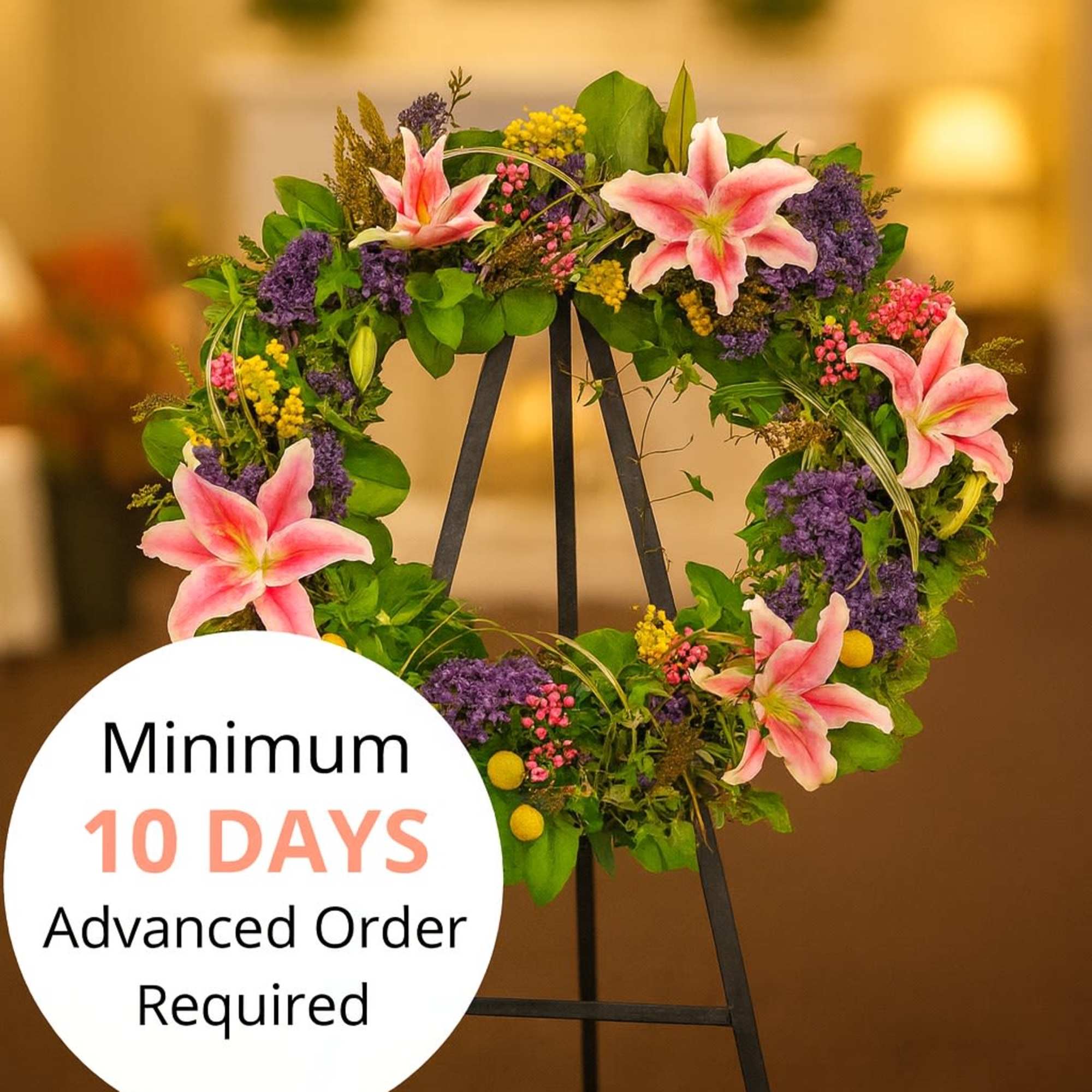 Standing wreath with pink lilies and mixed purple and yellow flowers on a black easel.