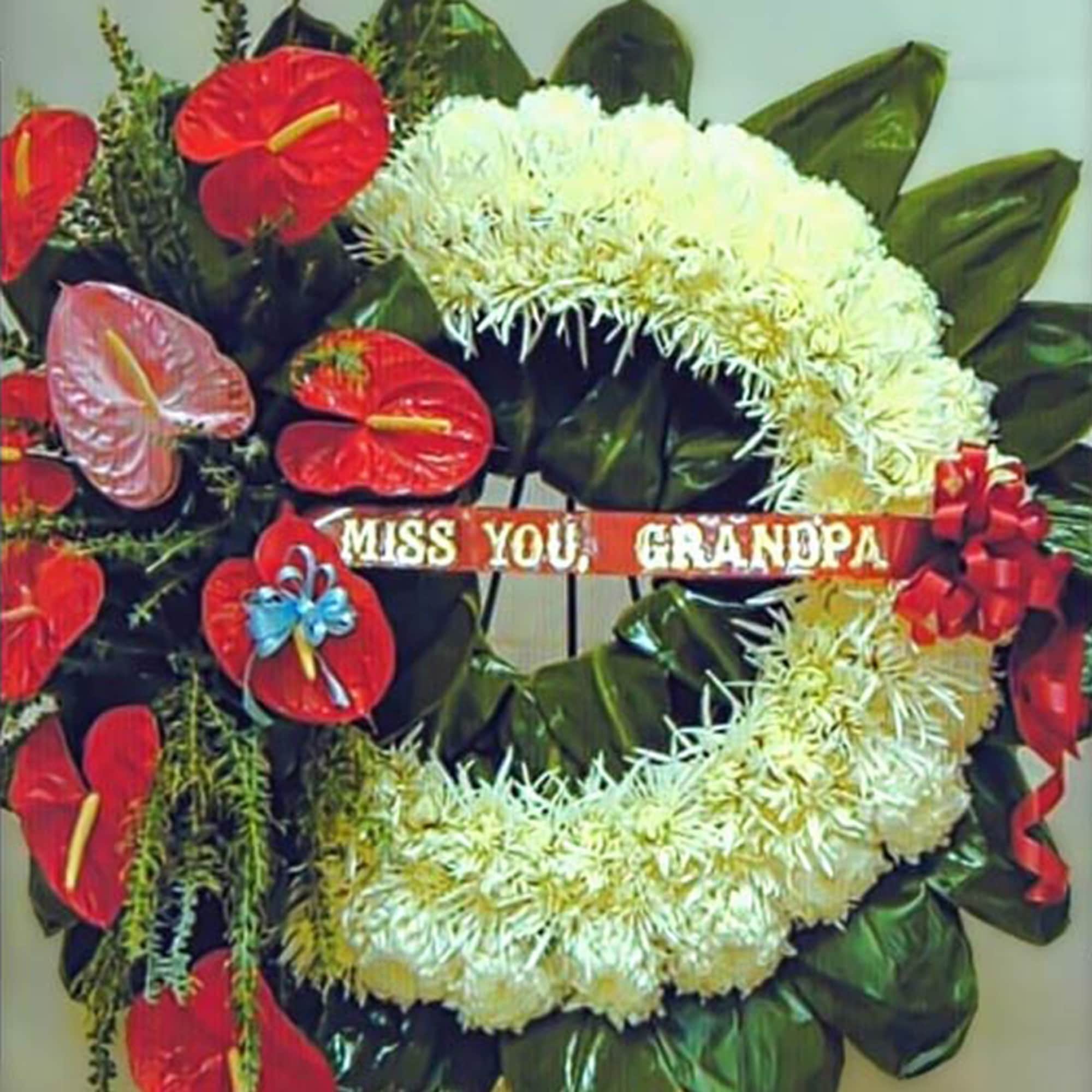 Standing funeral wreath of white flowers with red accent blooms and a 'Miss You, Grandpa' ribbon