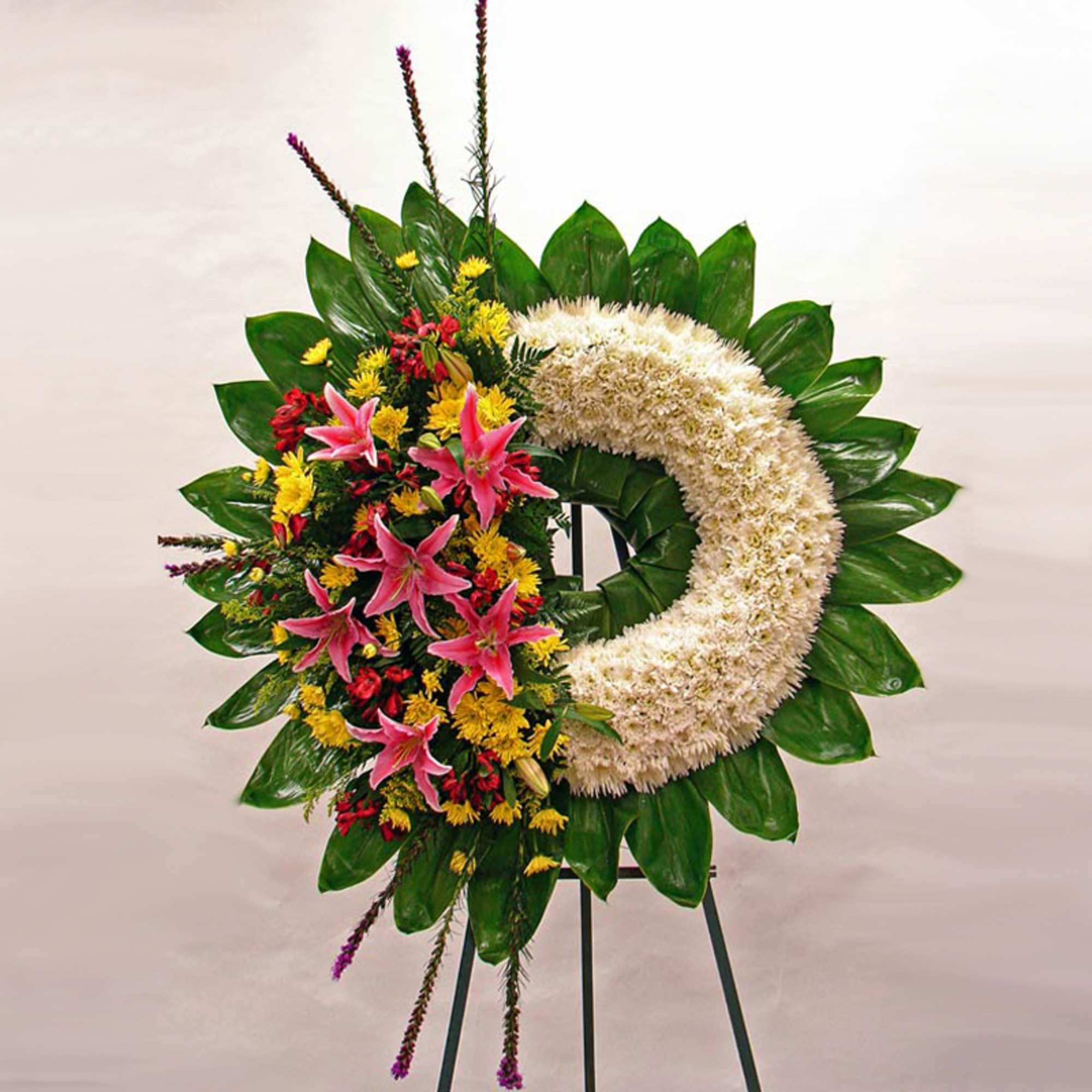 Large white floral wreath with green leaves and pink lilies on a standing easel