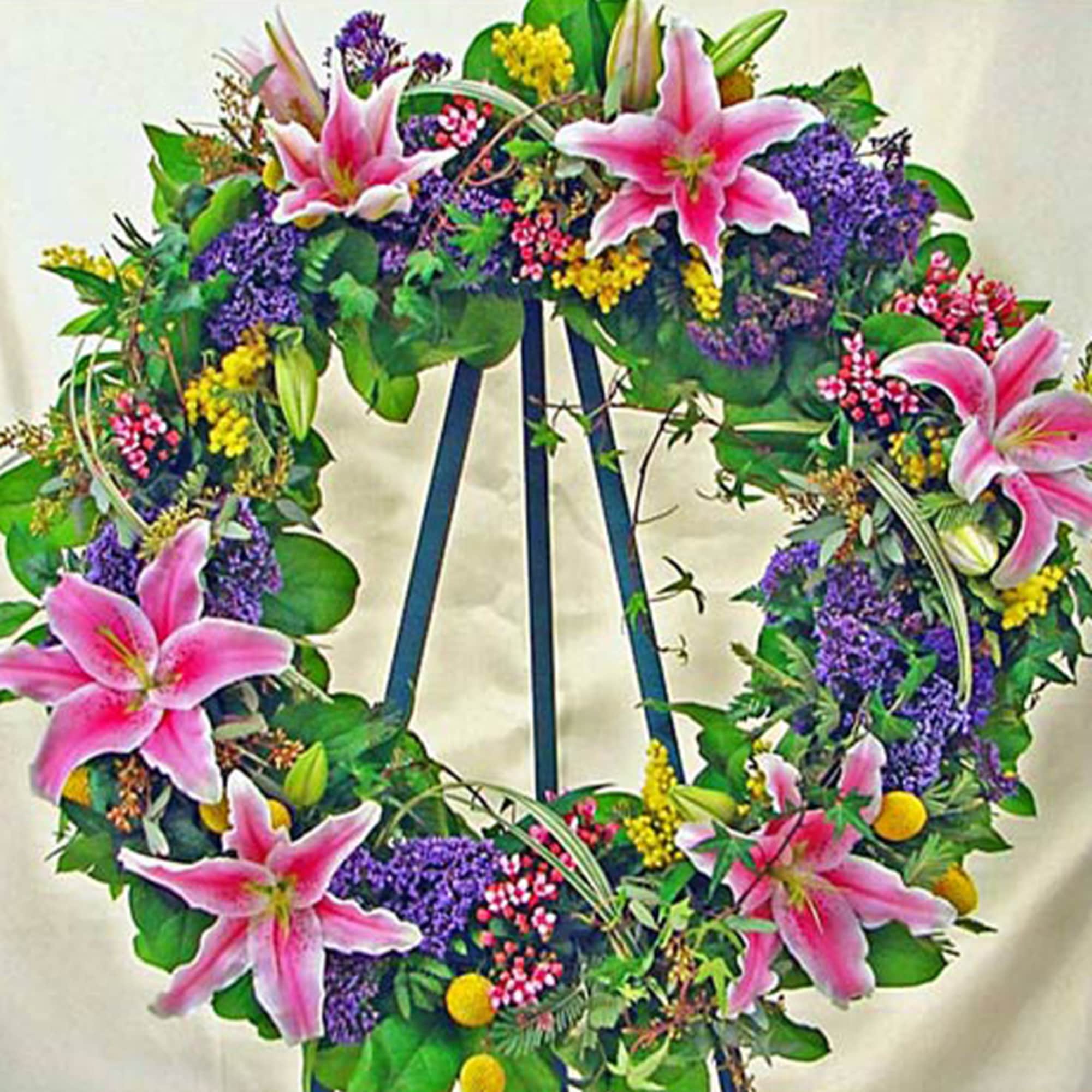 Standing wreath of pink lilies and mixed colorful flowers displayed on a metal easel.
