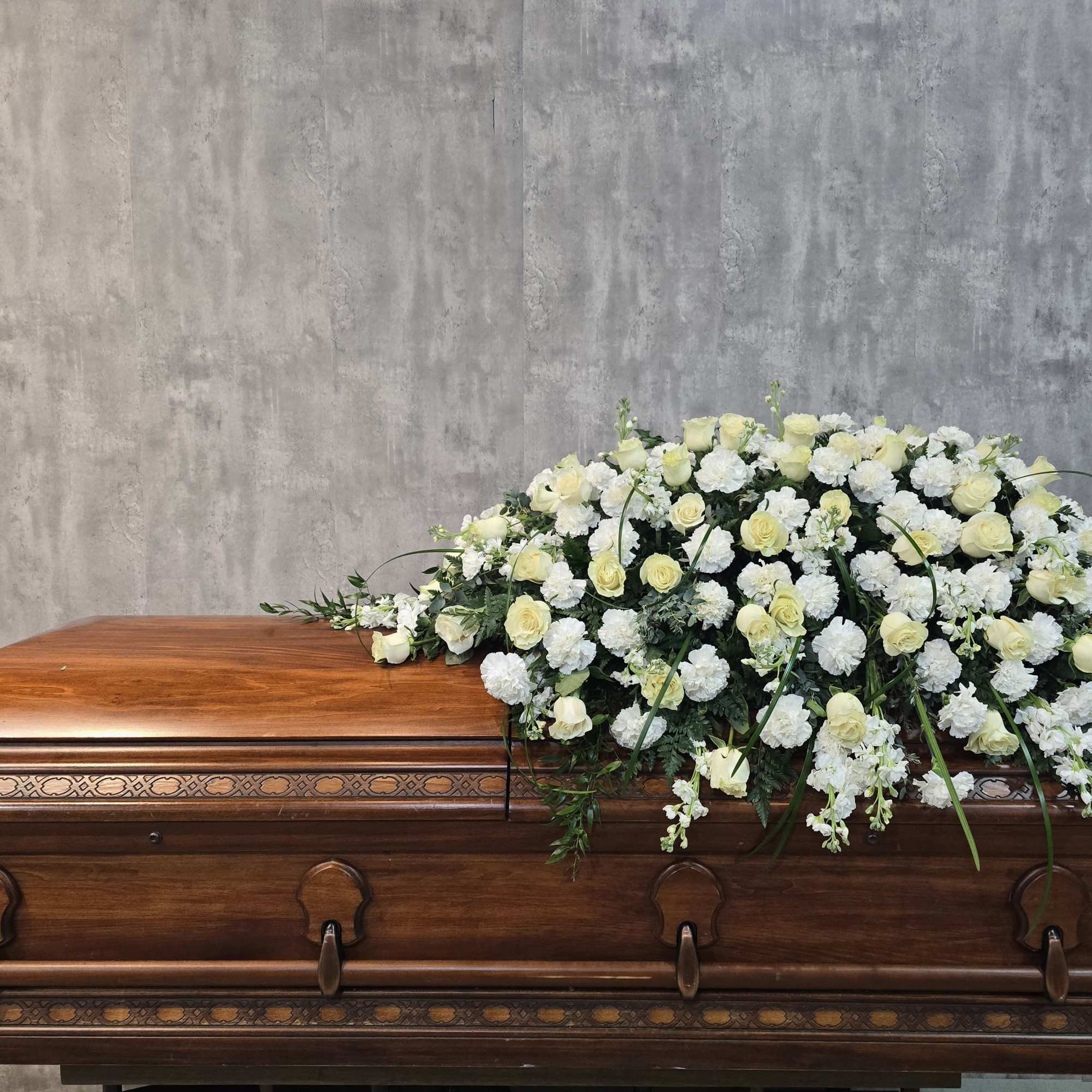 White and pale yellow floral spray on a wooden casket