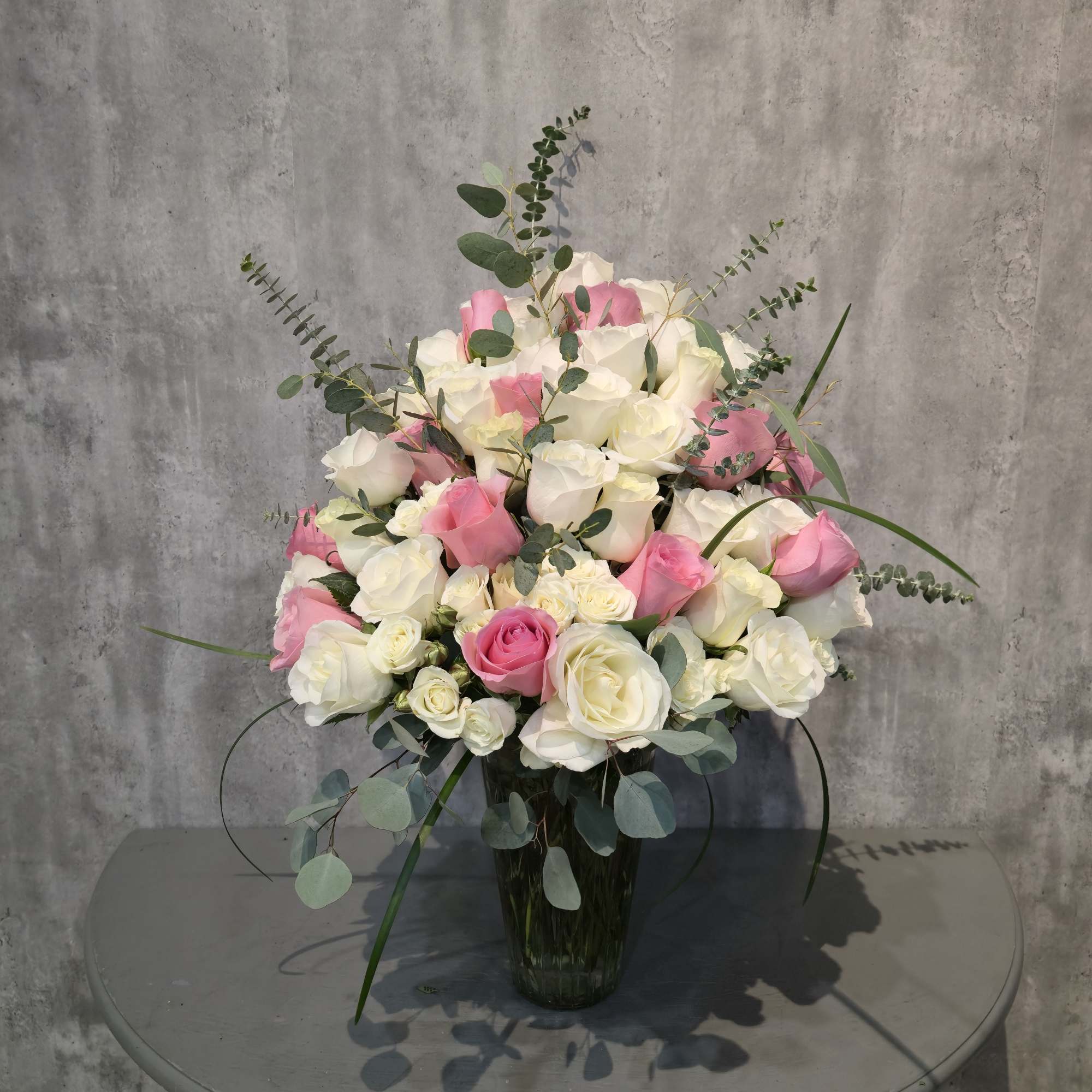 A dense cluster of pink and white roses arranged in a clear, photo 2 of 2