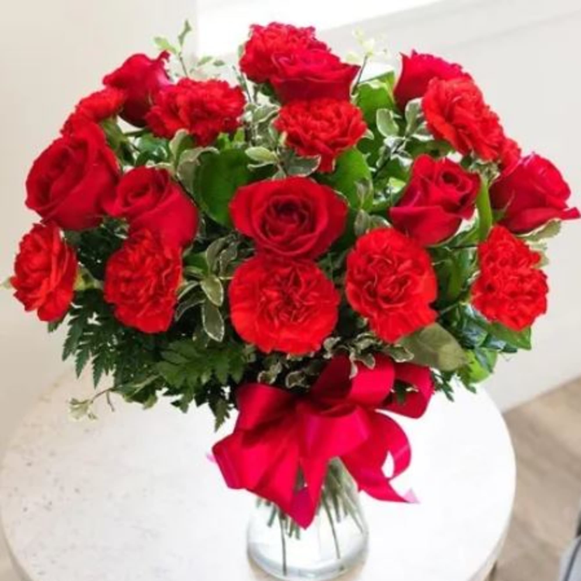 Bouquet of red roses and carnations in a clear glass vase with a red ribbon