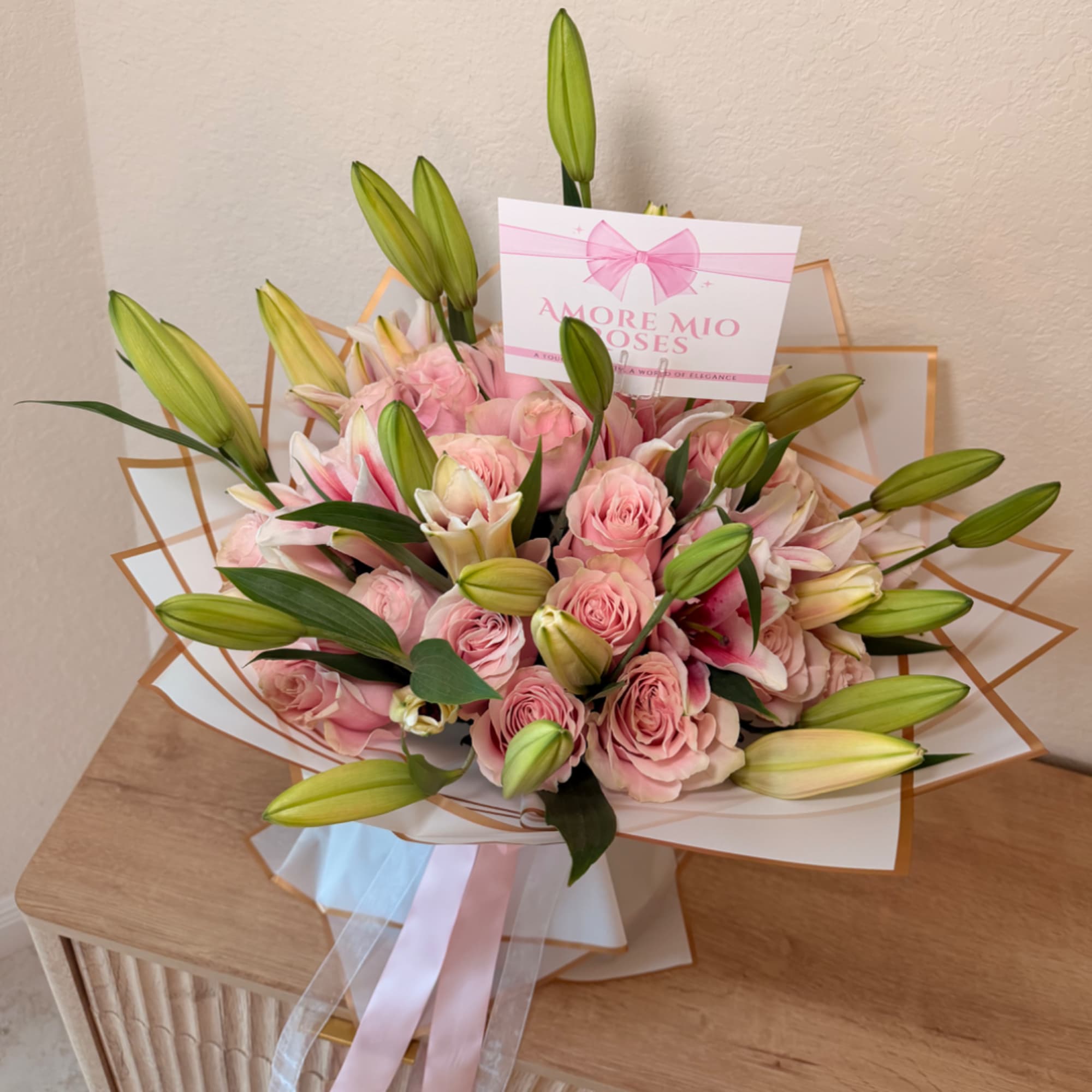 Pink roses and lilies arranged in a wrapped bouquet with a pink ribbon