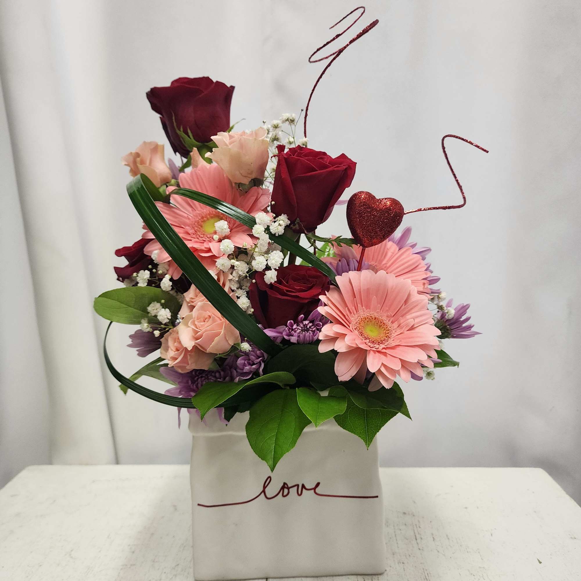 Pink and burgundy flower arrangement in a white box with a heart pick