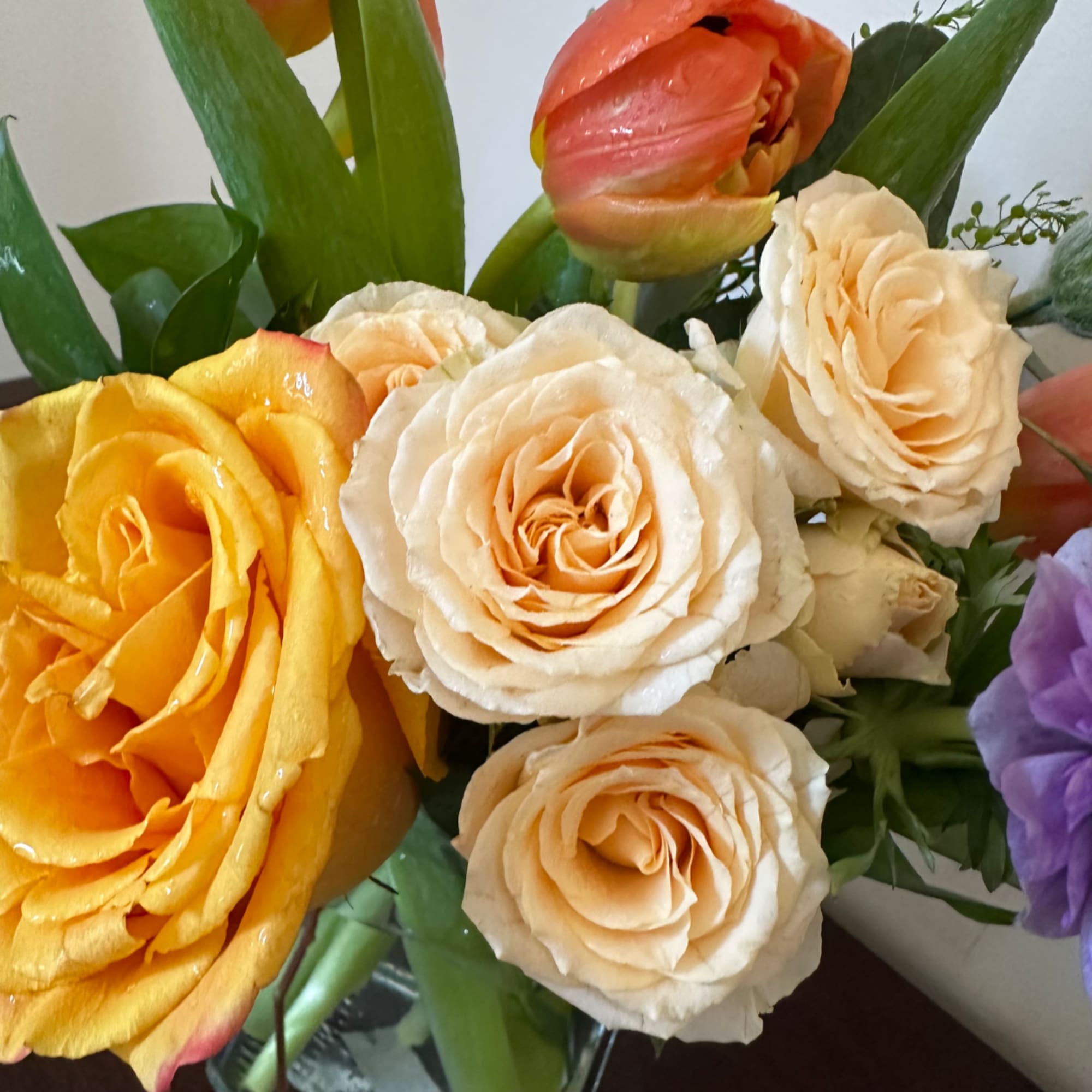 Bouquet of yellow, cream, and peach roses with a pink tulip and purple bloom