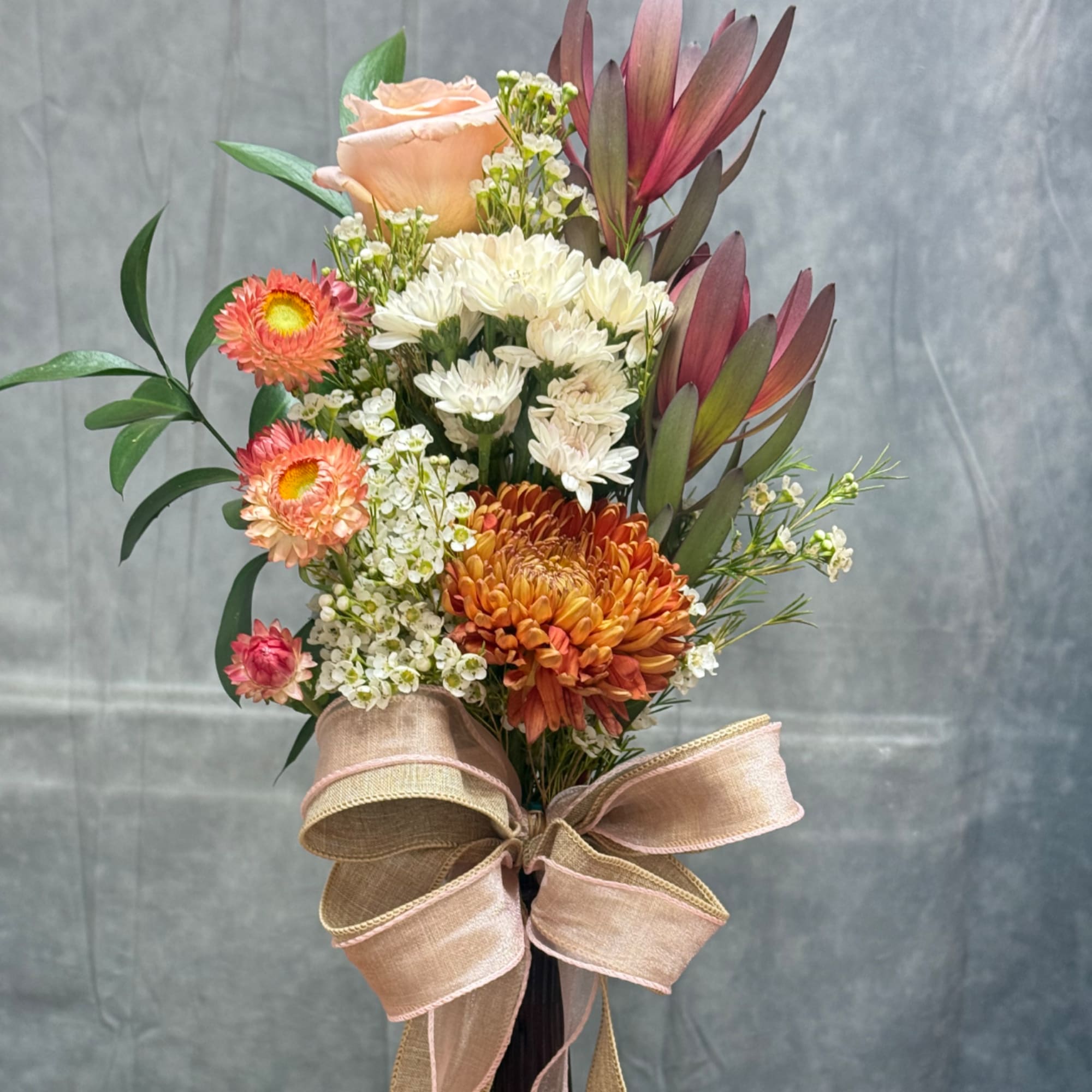 Mixed bouquet with peach rose, white chrysanthemums, and orange blooms tied with a large ribbon