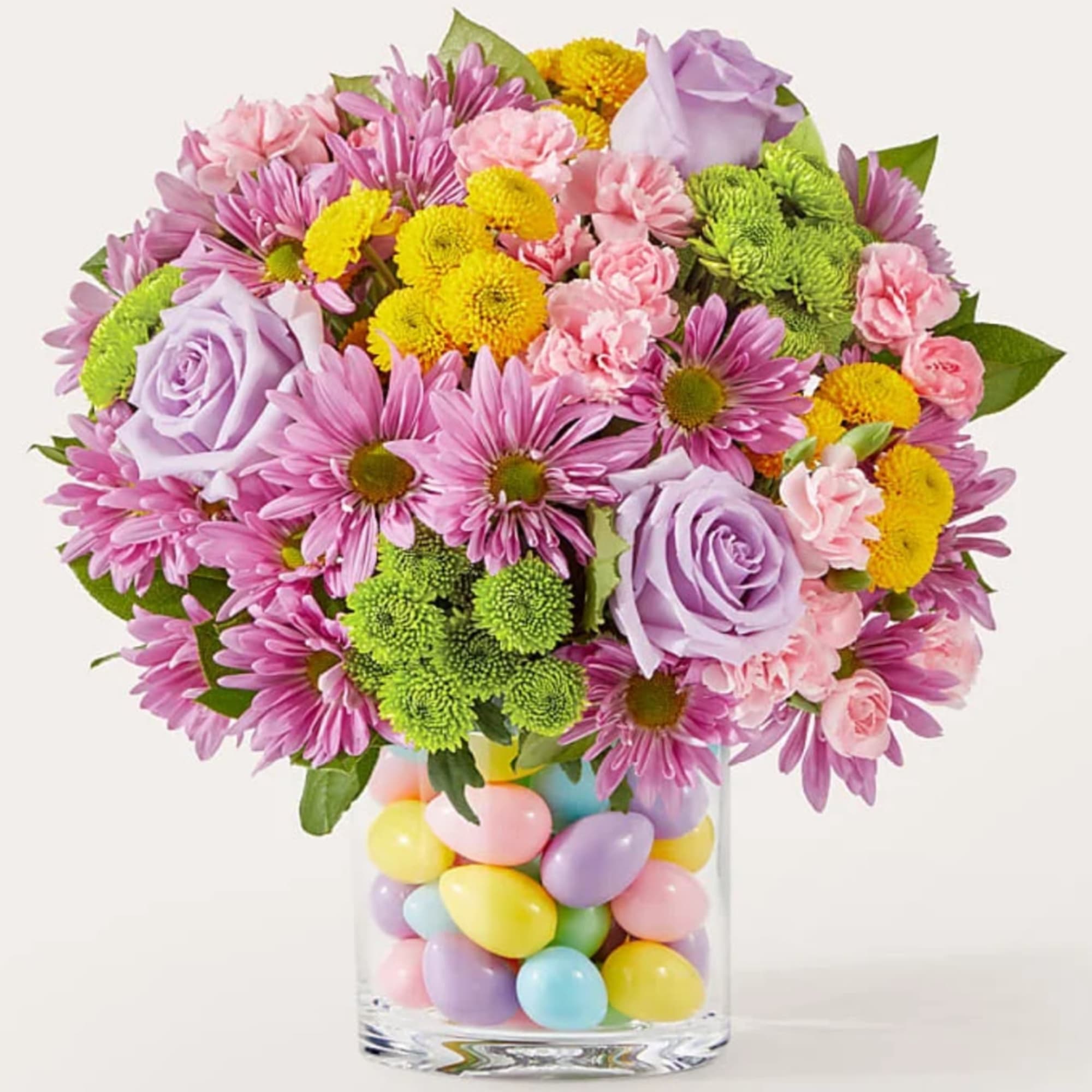 Pink and lavender flowers in a glass vase filled with pastel eggs