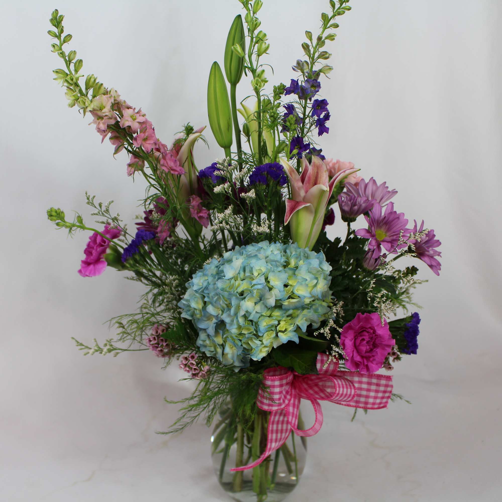 Tall mixed bouquet in a glass vase with blue hydrangea and pink ribbon