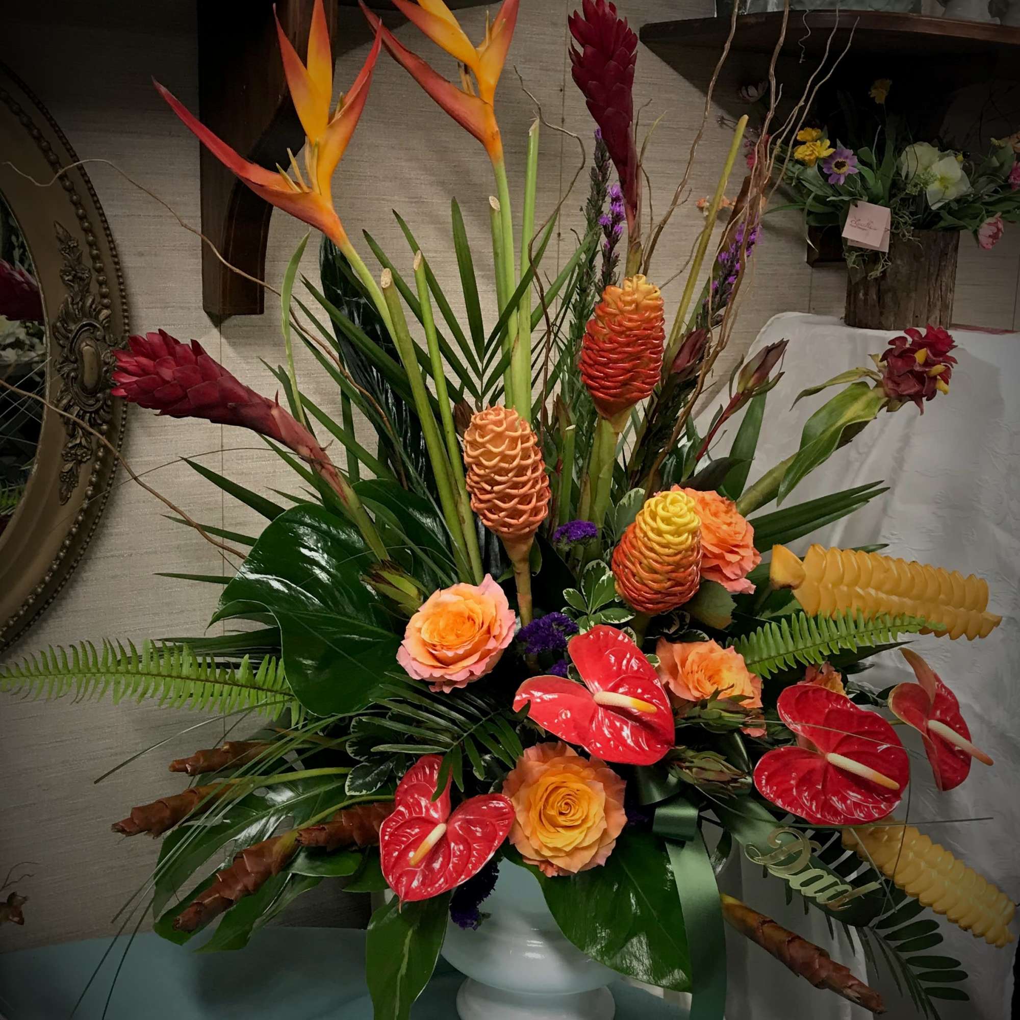 Tropical floral arrangement with orange birds of paradise and red anthuriums in a white vase