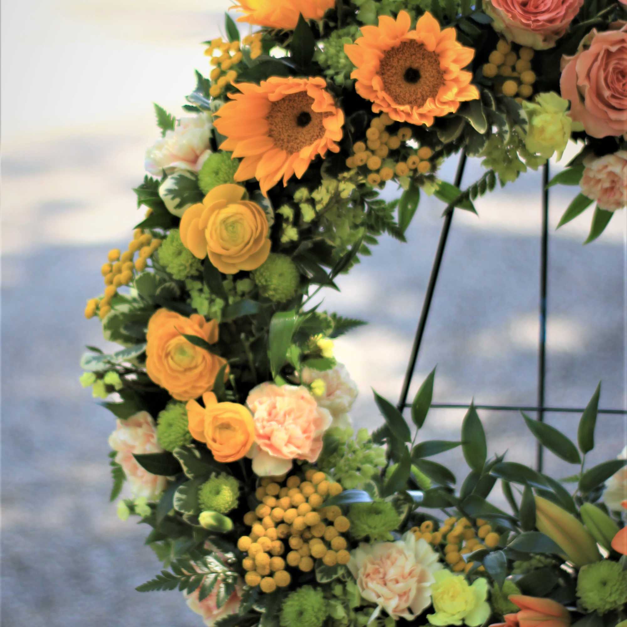 Floral wreath with orange sunflowers and peach roses on a black stand